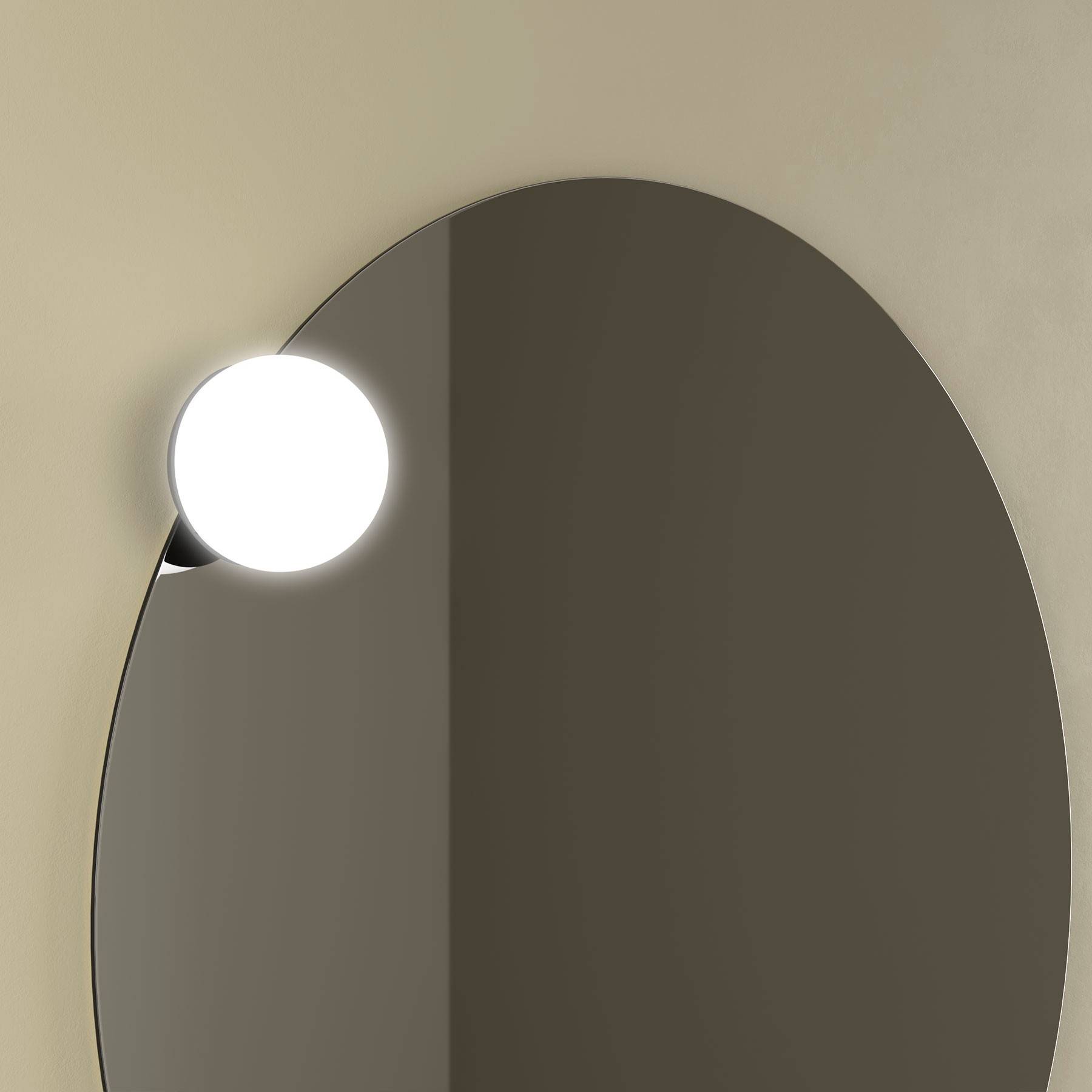Ein ovaler Spiegel, der an einer beigen Wand hängt, mit einer runden, leuchtenden Lichtarmaturen, die in der oberen linken Ecke befestigt ist.
