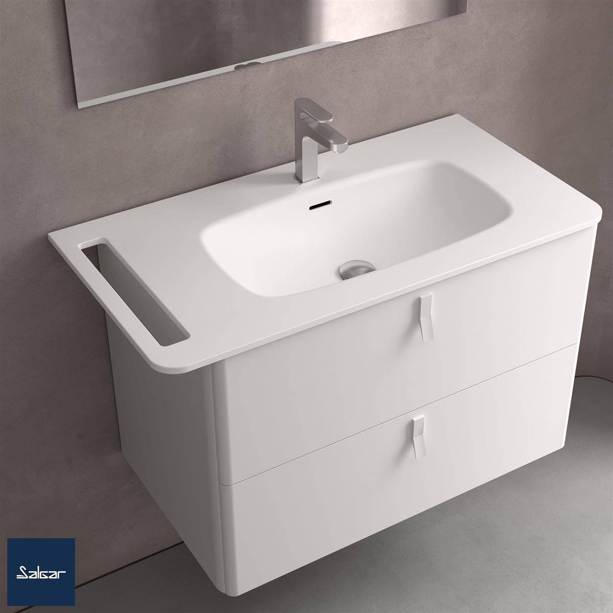 Modernes weißes Badezimmerwaschtisch mit integriertem Waschbecken, einfacher Armatur, seitlichem offenem Regal und zwei Schubladen an einer grauen Wand.
