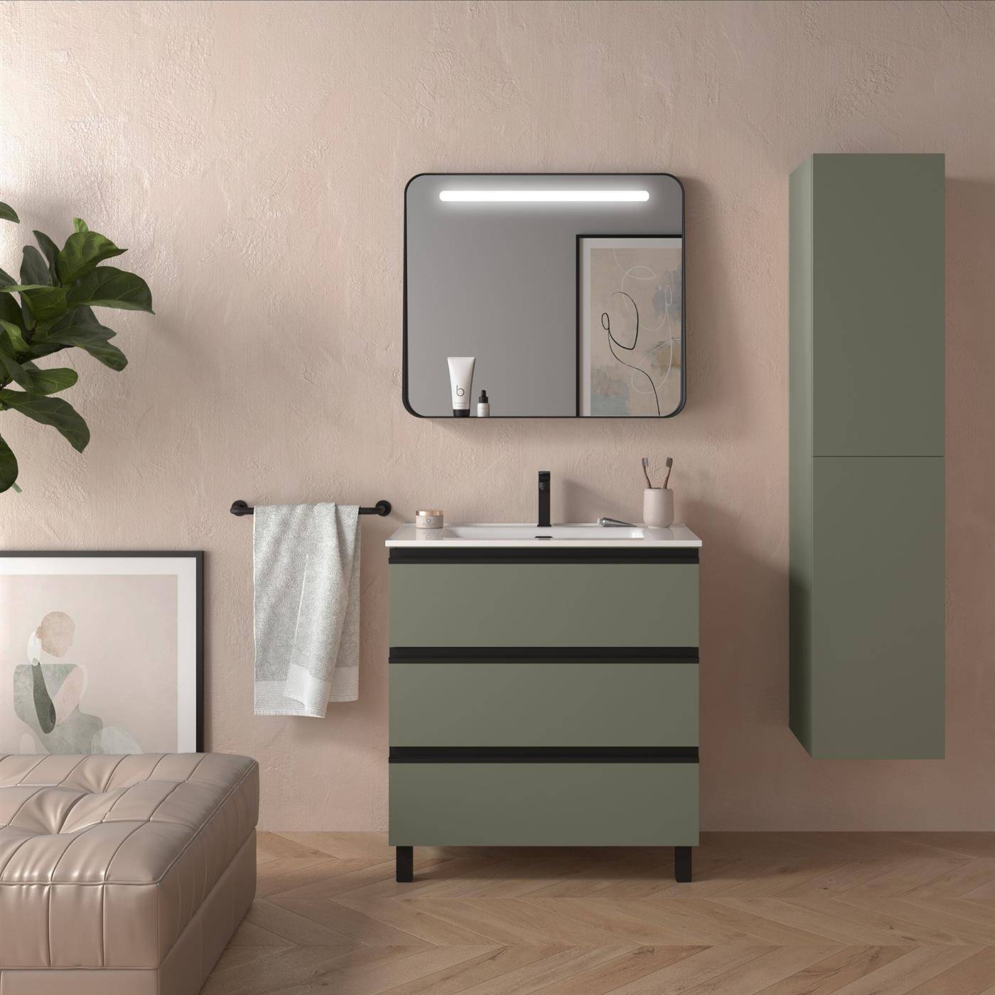 Modernes Badezimmer-Waschtisch mit olivgrünen Schränken, Wandspiegel und Leuchte, Handtuchstange, gerahmter Kunstwerk und passender hoher Wandschrank vor einer beigefarbenen Wand.