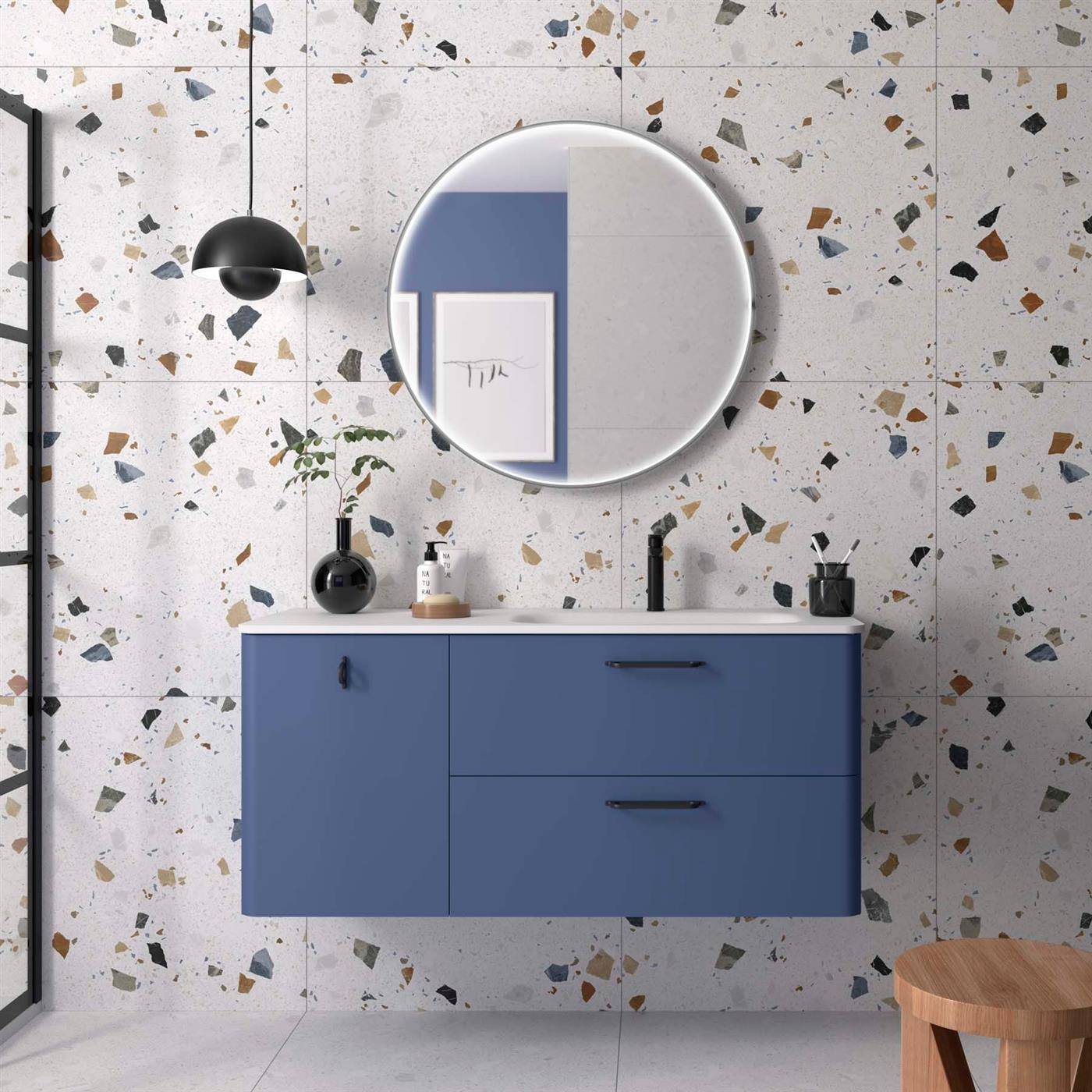 Moderne Badezimmervantiy mit blauer Wandmontage-Schrank, rundem Spiegel, schwarzen Wandleuchten und Terrazzofliesen-Wand.