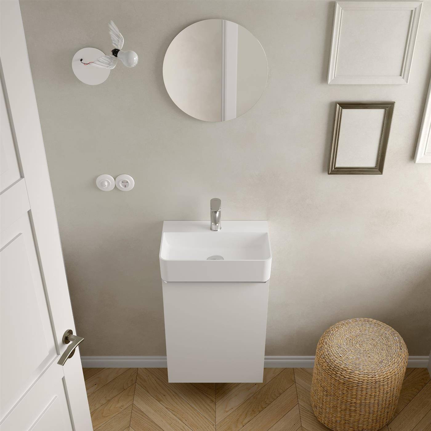 Minimalistisches Badezimmer mit wandmontiertem Waschbecken, rundem Spiegel, gerahmten Wandbildern und geflochtenerem Hocker neben einer weißen Tür.