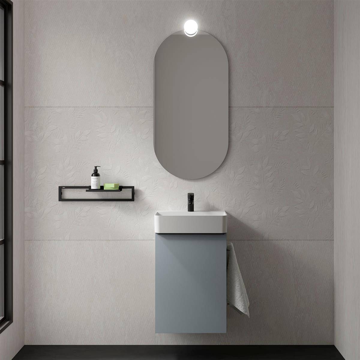 Modernes Badezimmer-Waschtisch mit ovalem Spiegel und Wandleuchte über einem schwebenden blauen Schrank, plus ein Regal mit Seife und Flasche.