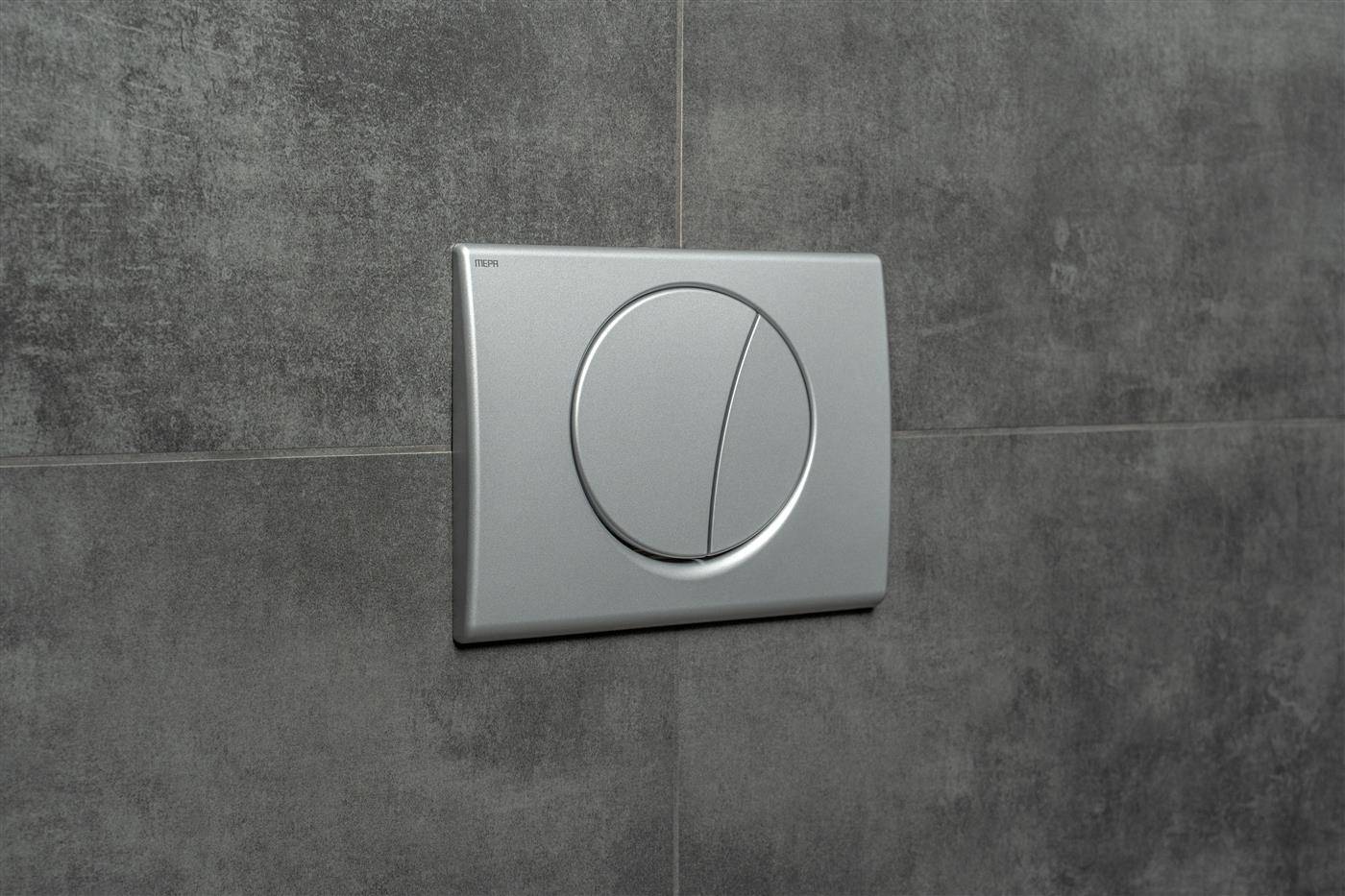 Eine silberfarbene Dual-Spül-Toilettenplatte an der Wand montiert auf einer dunkelgrauen gefliesten Wand.