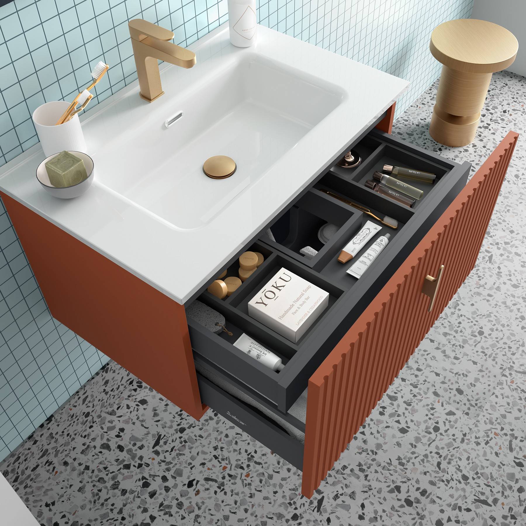 Orangefarbene Waschtischplatte mit Terrazzoböden, offene Schubladen mit sortierten Toilettenartikeln und einem Buch mit dem Titel ‚YOKU', daneben ein Holzhocker.