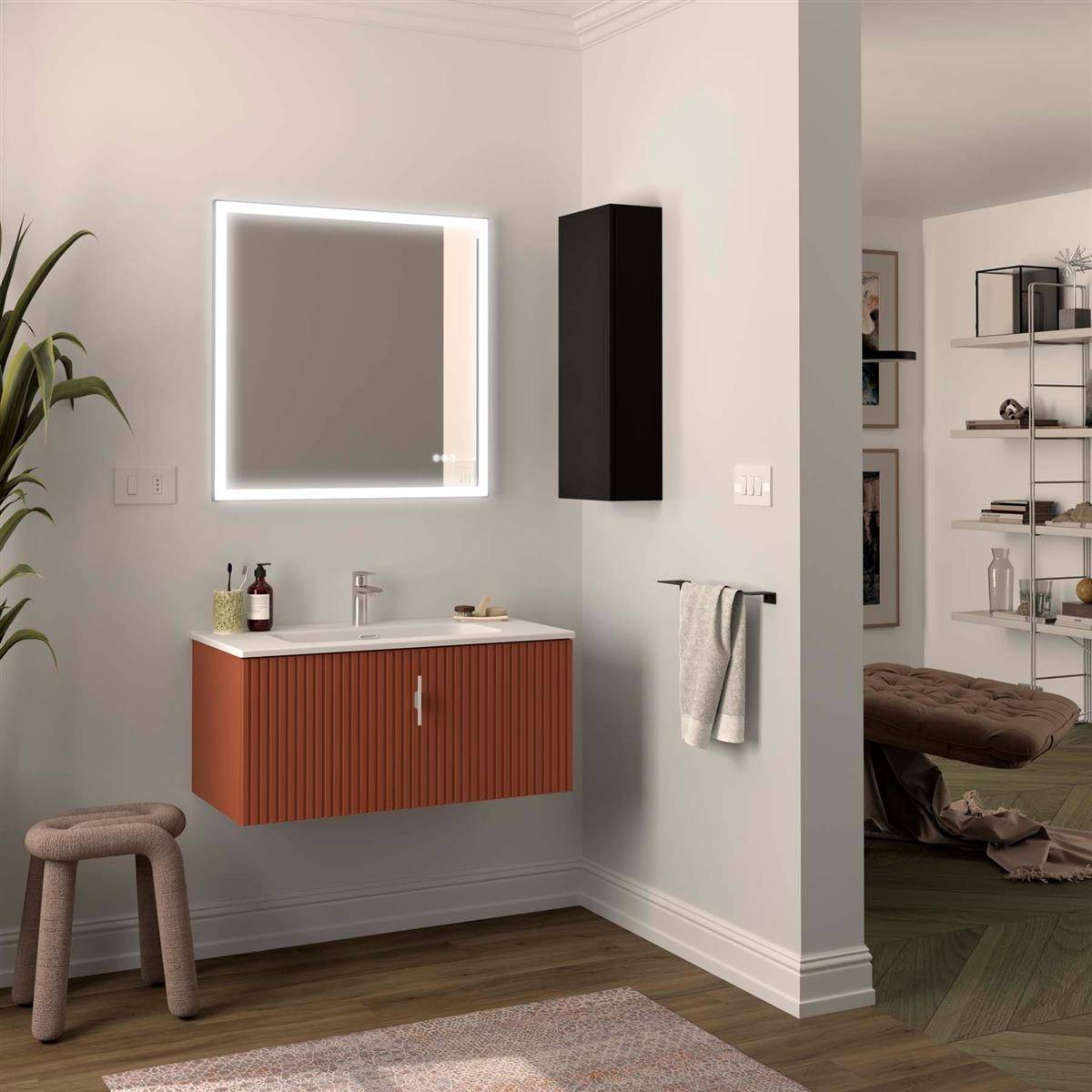 Modernes Badezimmermöbel mit beleuchtetem quadratischem Spiegel, orangefarbenem geripptem Schrank, Wandschrank, Handtuchstange und Hocker; angrenzender Schlafraum durch die Türöffnung sichtbar.