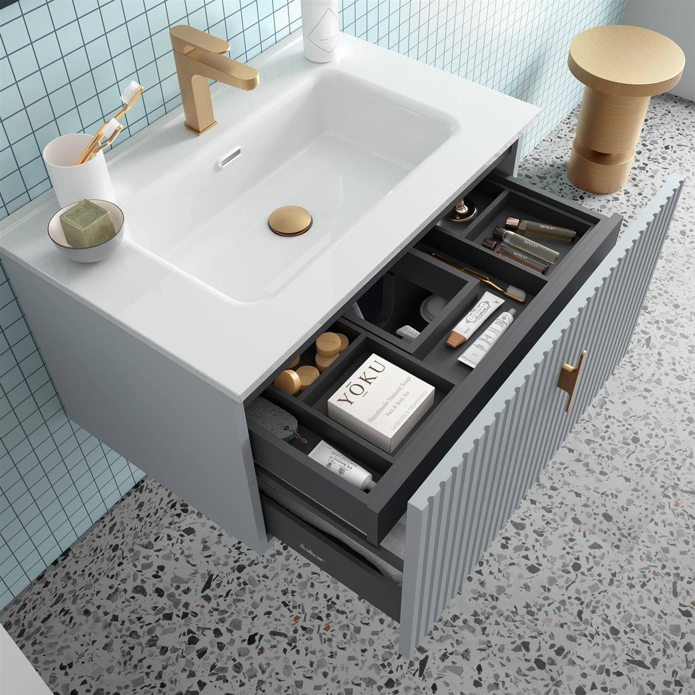 Modernes Badezimmerwaschtisch mit offenen Schubladen, die organisierte Toilettenartikel und Pflegeutensilien zeigen, weißes Waschbecken, goldfarbener Wasserhahn und passierender Holzhocker.