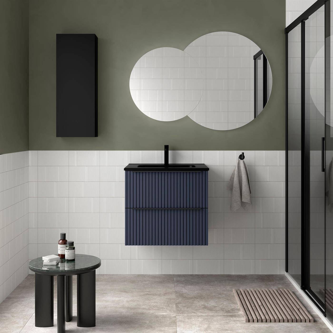Modernes Badezimmer mit wandmontiertem schwarzem Waschbeckenunterschrank, rundem Spiegel, Duschkabine und kleinem Beistelltisch mit Toilettenartikeln.