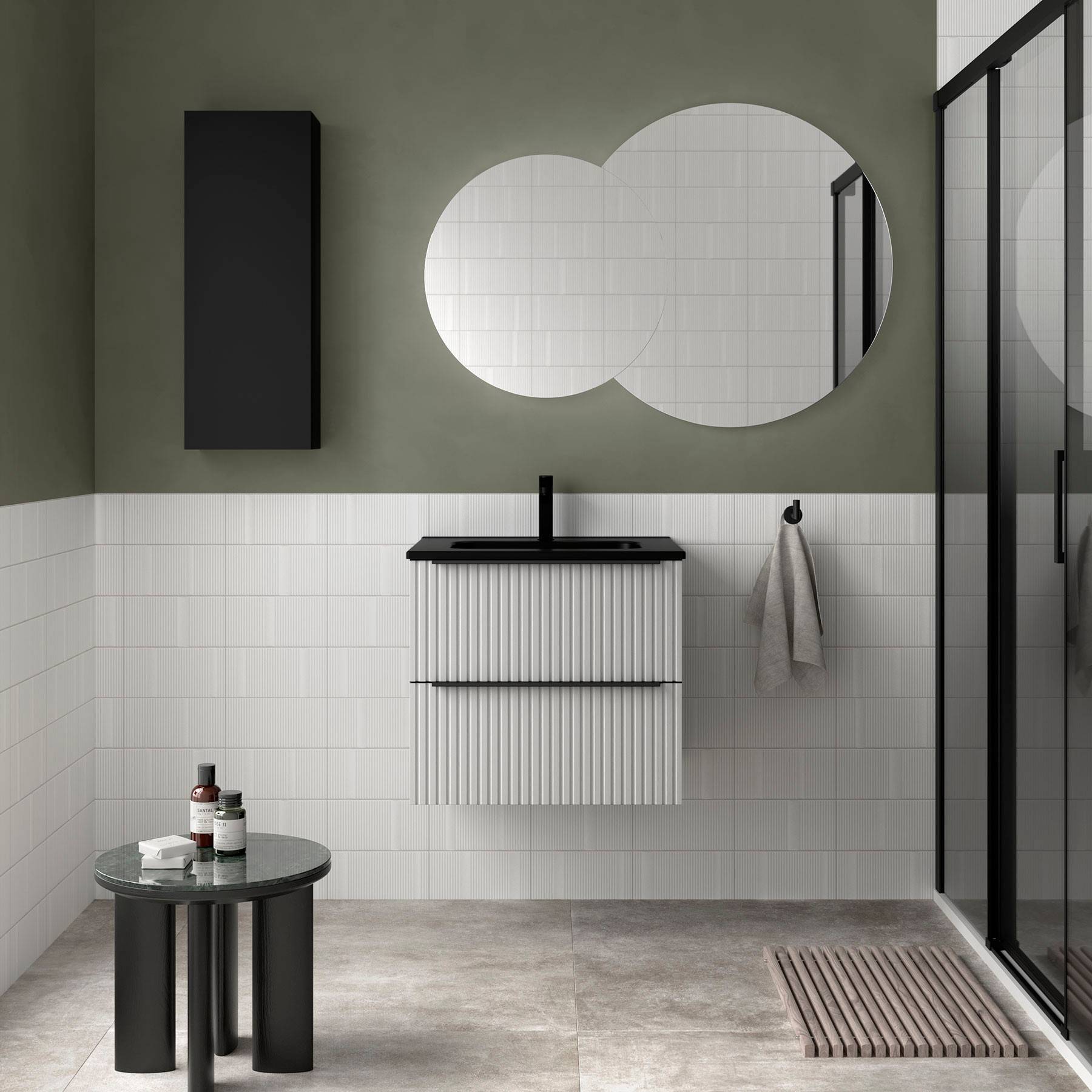 Modernes Badezimmer mit rundem Spiegel, schwarzem Unterschrank und neutralen Farbtönen. Ein kleiner Tisch mit Flaschen steht neben einer Glasdusche.