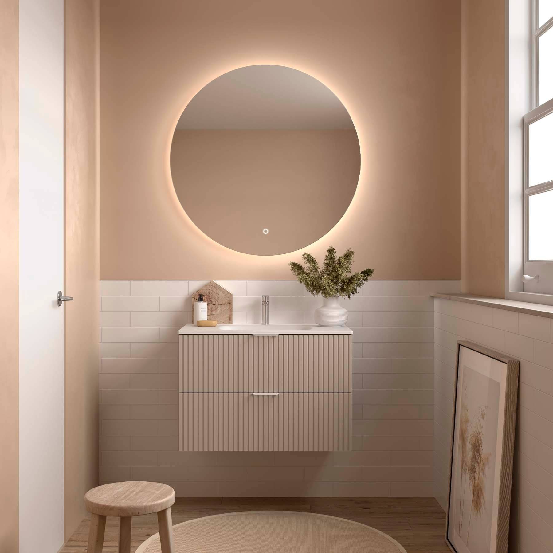 Minimalistisches Badezimmer mit rundem beleuchtetem Spiegel, beigen Wänden und einem kleinen Holzwaschtisch mit einer Pflanze. Natürliches Licht von einem Fenster.