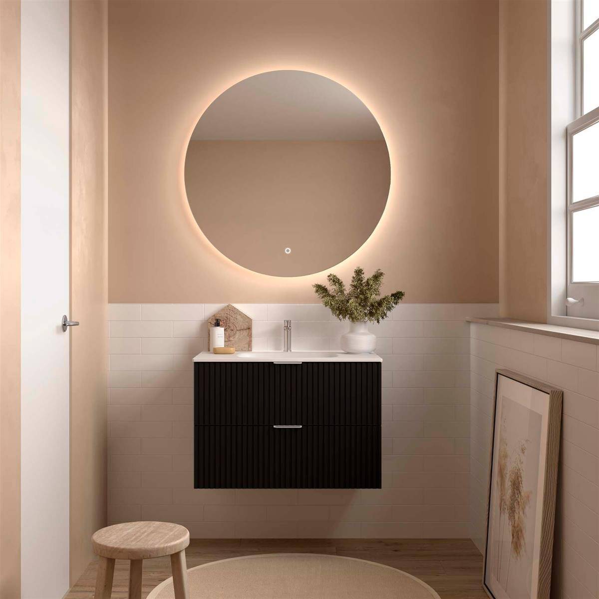 Modernes Badezimmer mit an der Wand montiertem schwarzem Waschtisch, rundem hinterleuchtetem Spiegel, Waschbecken, Hocker und lehnendem Rahmenbild am Fenster.