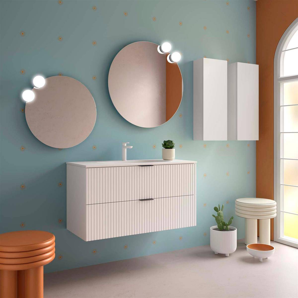 Modernes Badezimmerinterieur mit schwebendem weißem Waschtisch, zwei runden beleuchteten Spiegeln, Wandschrank, Pflanzen und orangefarbenen Akzenthockern am Fenster.