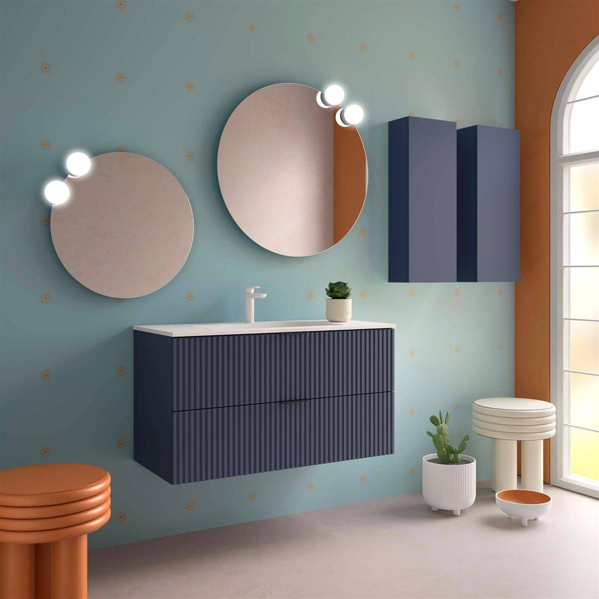 Modernes Badezimmerinterieur mit blauer Wand, zwei runden Spiegeln mit Beleuchtung, schwebendem Waschtisch, Wandschrank, Hockern, Pflanzen und einem hohen Fenster.
