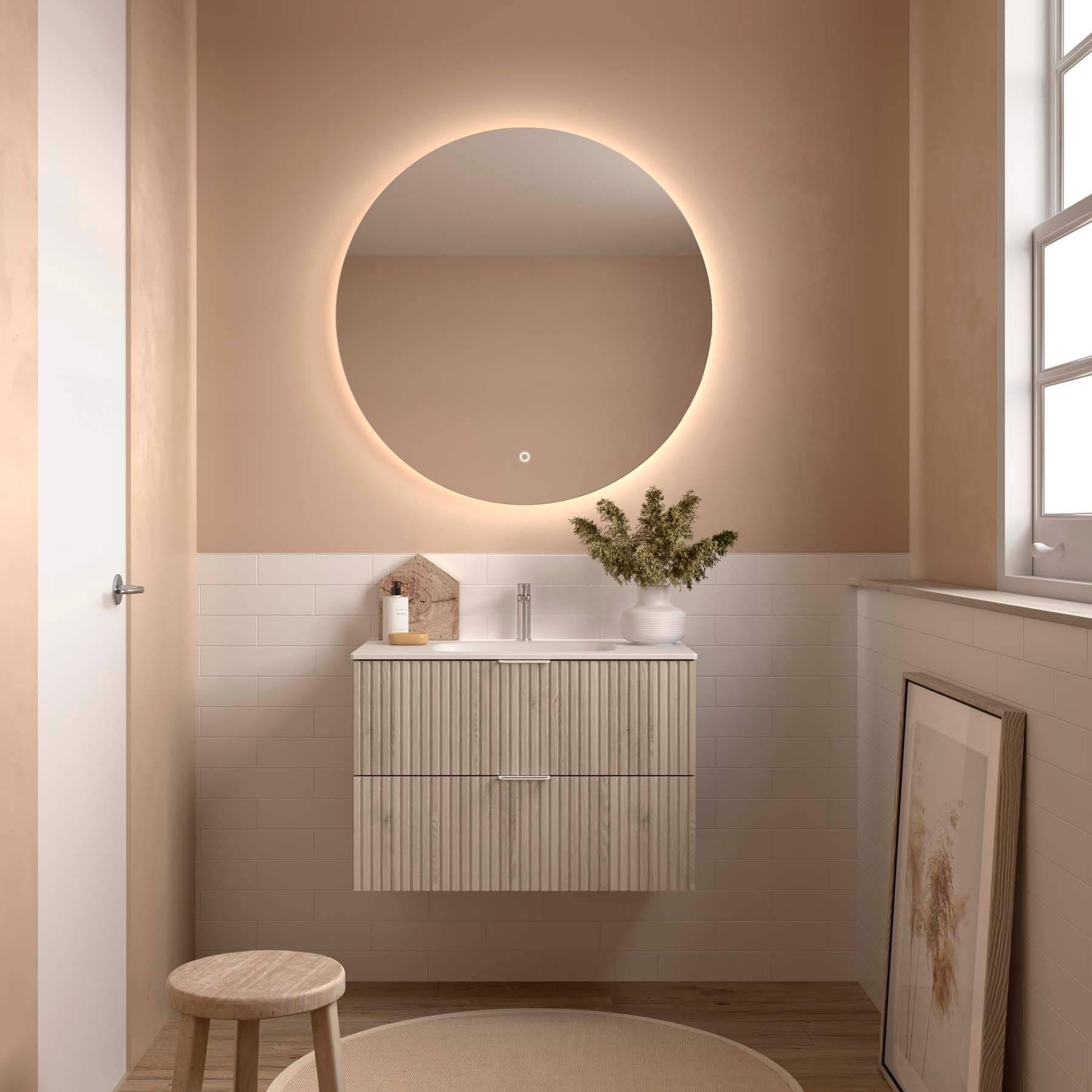 Zeitgenössisches Badezimmer mit einem kreisrunden, hintergrundbeleuchtetem Spiegel, beigen Wänden und einem Holzwaschbeckenunterschrank. Ein rundes Hocker und gerahmte Kunst vervollständigen die Dekoration.