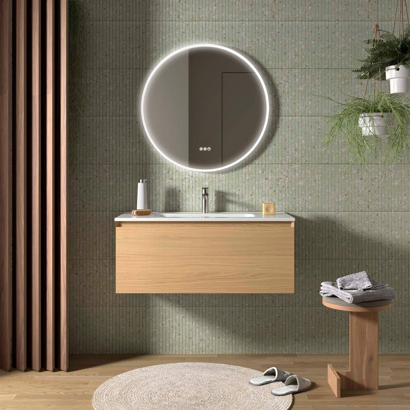 Modernes Badezimmer-Waschtisch mit rundem beleuchteten Spiegel, wandmontiertem Holz-Waschbeckenunterschrank, Handtuchhocker, Hausschuhen und hängender Pflanze an der gefliesten Wand.