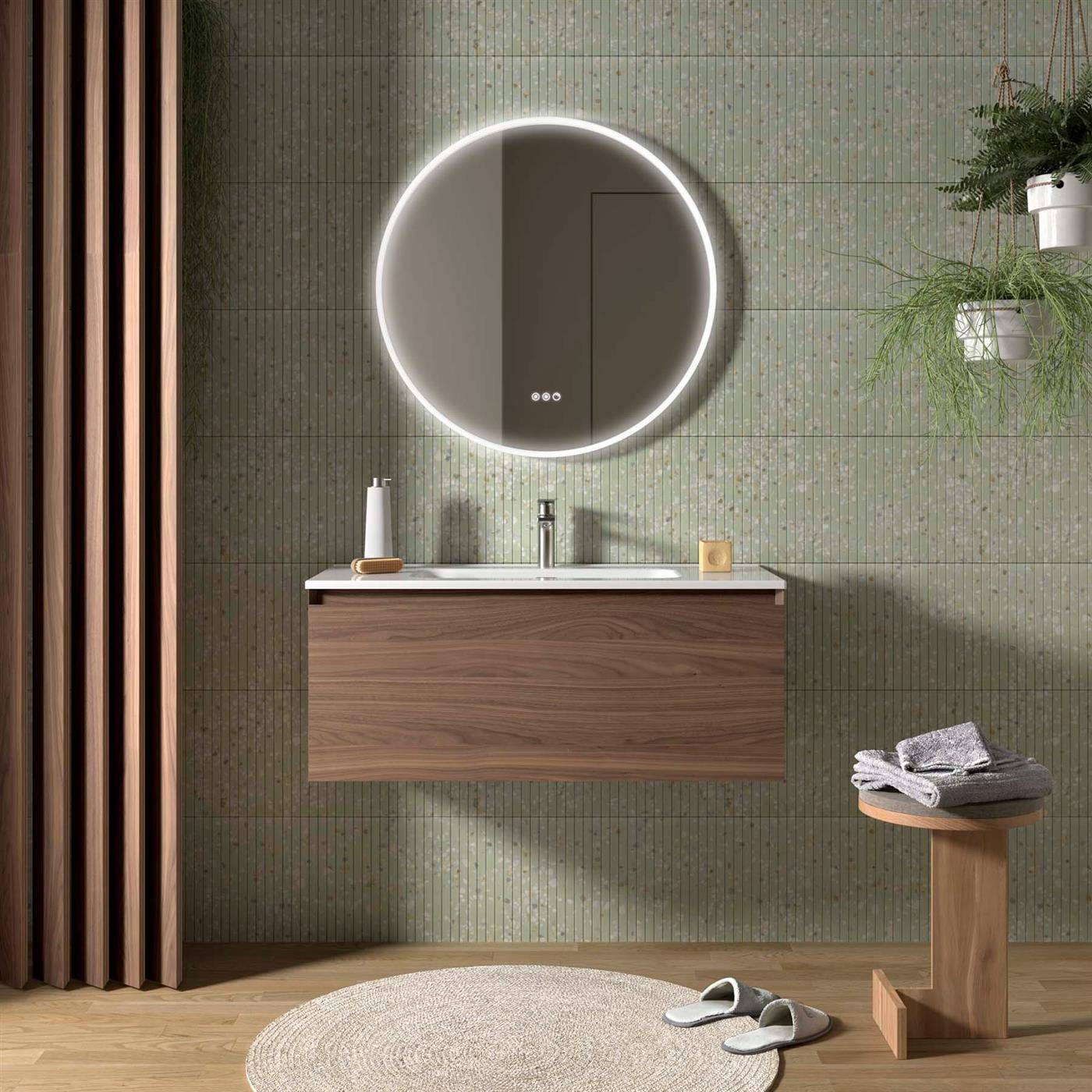 Modernes Badezimmer mit rundem beleuchtetem Spiegel über einem schwebenden Holzwaschbecken, grüner Fliesenwand und Handtüchern auf einem Hocker.