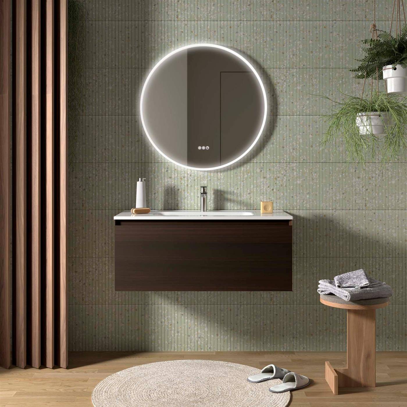 Modernes Badezimmer mit einem runden hinterleuchteten Spiegel über einem wandmontierten Waschtischunterschrank, Holzboden, Handtücher auf einem Hocker und Hausschuhe auf dem Boden.