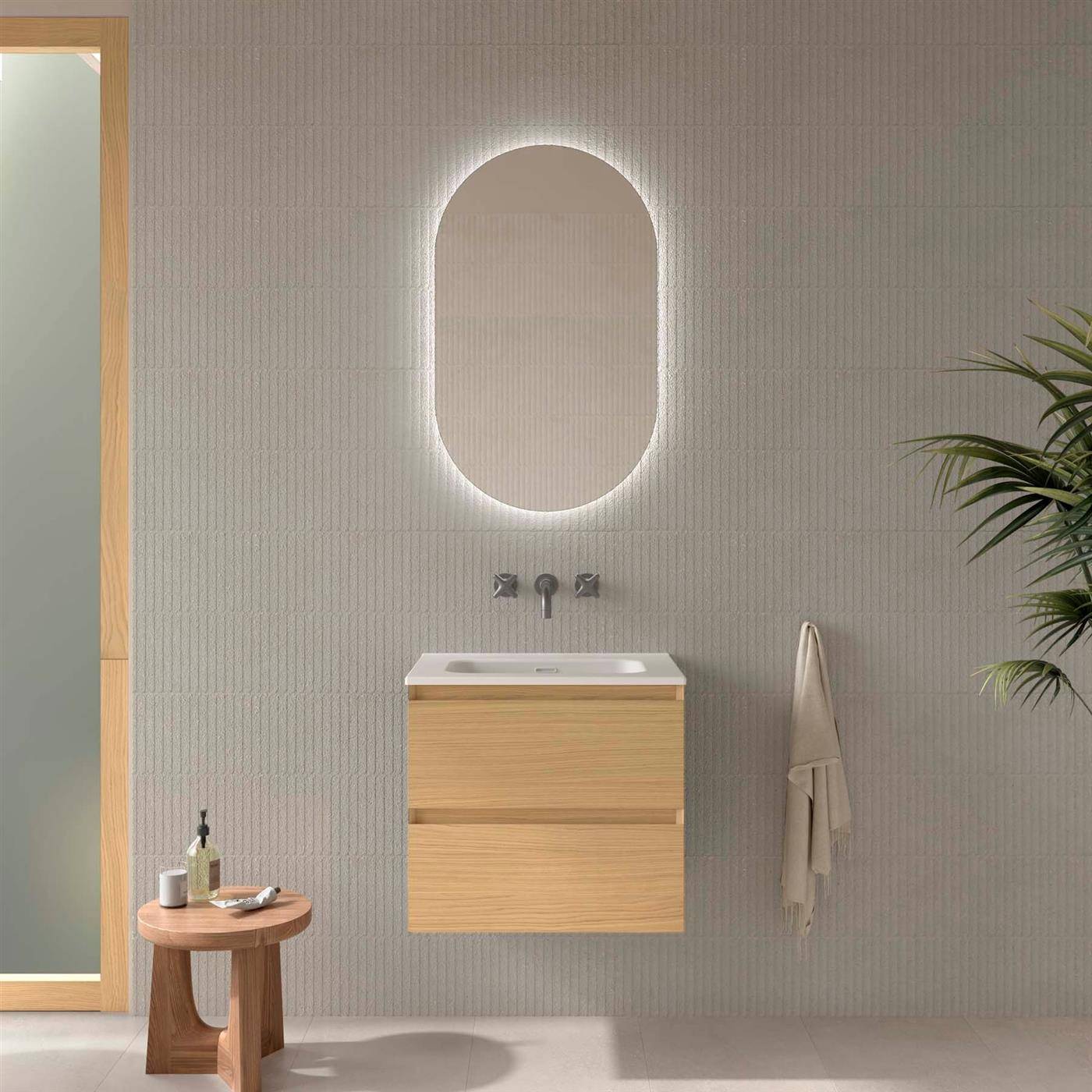 Modernes minimalistisches Badezimmer mit schwebendem Holzwaschtisch, beleuchtetem ovalem Spiegel, Wandarmatur, Handtuch, Seitenhocker und Pflanze.