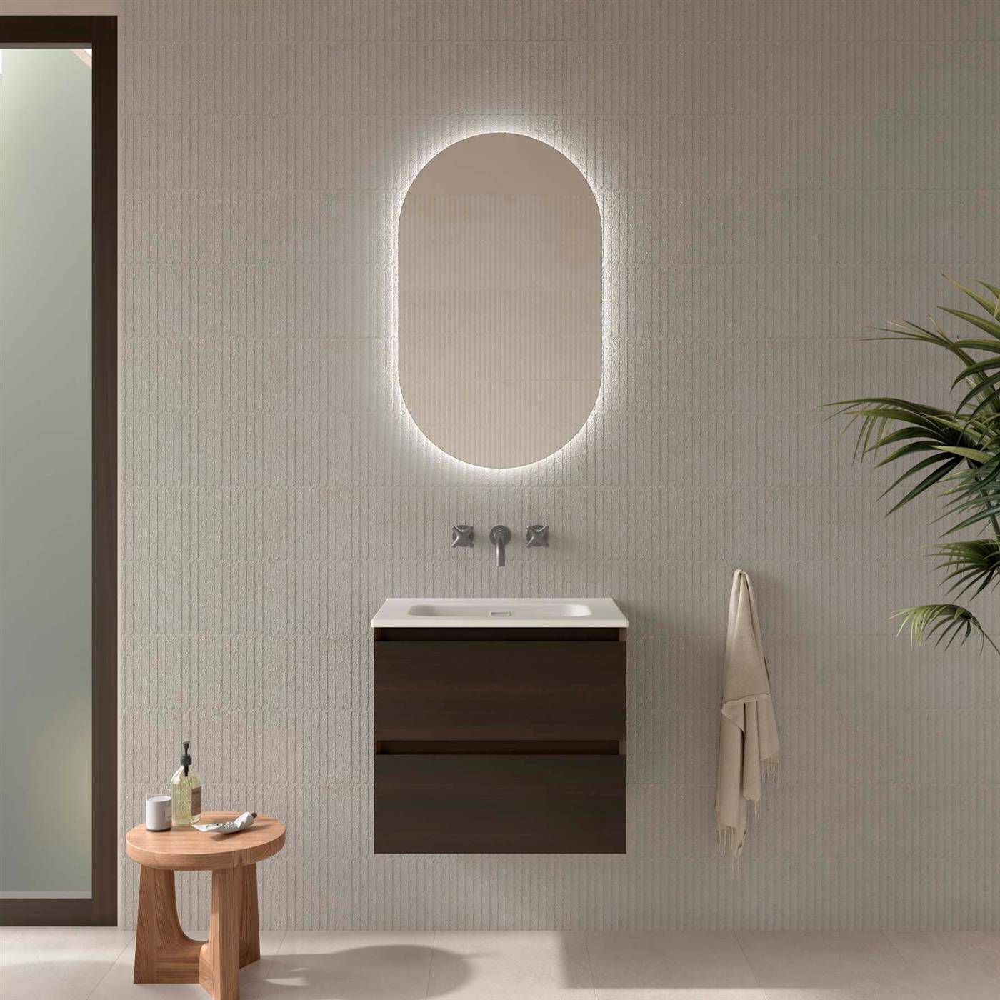 Modernes minimalistisches Badezimmer mit wandhängender Spüle und ovalem Hintergrundlicht-Spiegel, plus Beistelltisch, Handtuch und Pflanze.