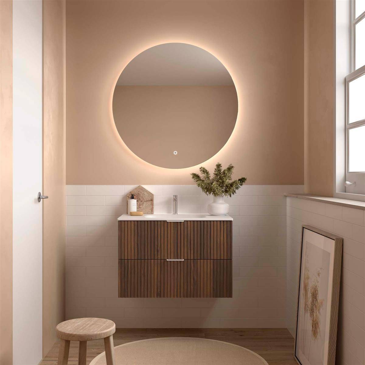 Modernes Badezimmer-Waschtisch mit rundem beleuchteten Spiegel, Holzschrank, Waschbecken, Hocker und gerahmter Kunst in einem beigen, minimalistischen Raum.
