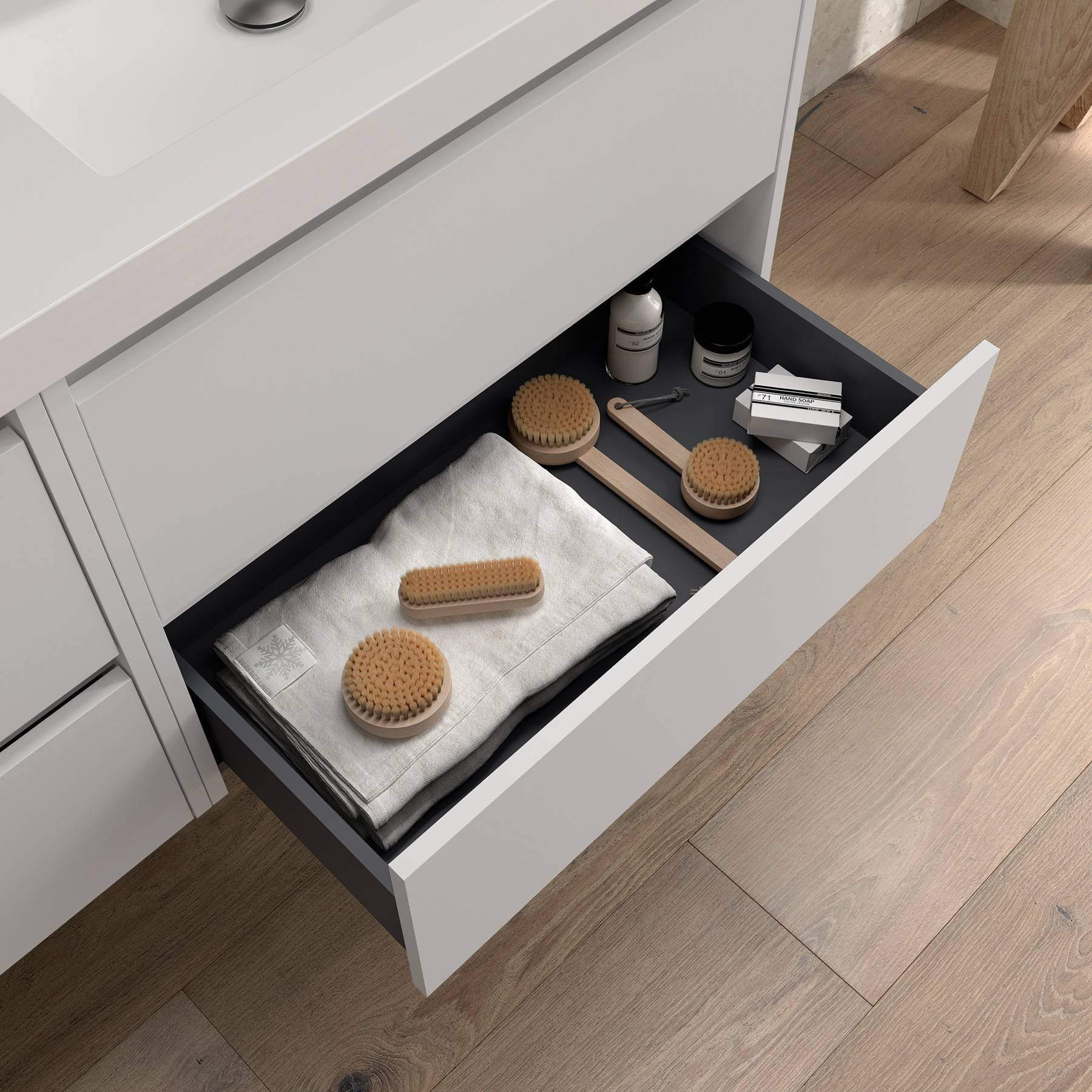 Badezimmerschublade geöffnet, zeigt ordentlich angeordnete Toilettenartikel, Bürsten und gefaltete Handtücher, neben einem Waschbecken auf der Ablage.