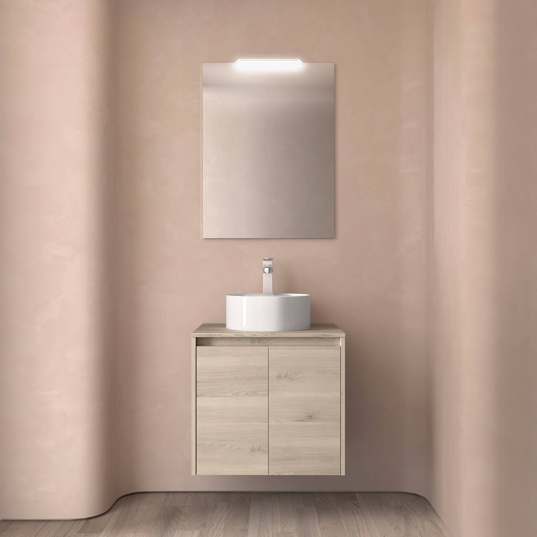 Ein minimalistisches Badezimmer zeigt ein rundes weißes Waschbecken auf einem Holzwaschtisch mit einem beleuchteten Spiegel darüber, vor einem Hintergrund von zarten rosa Wänden und Boden.
