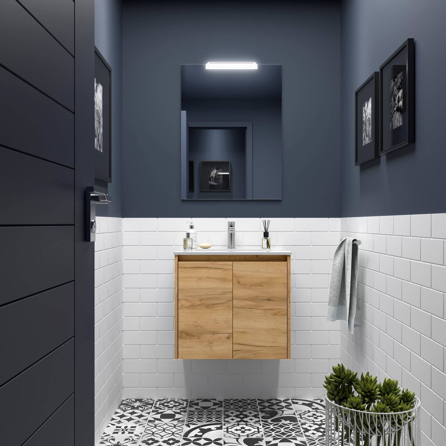 Ein kleines Badezimmer mit weißen Ziegelfliesen, einem Holzwaschtisch, einem Spiegel und gerahmten Bildern an einer dunklen Wand. Ein Handtuch hängt rechts.