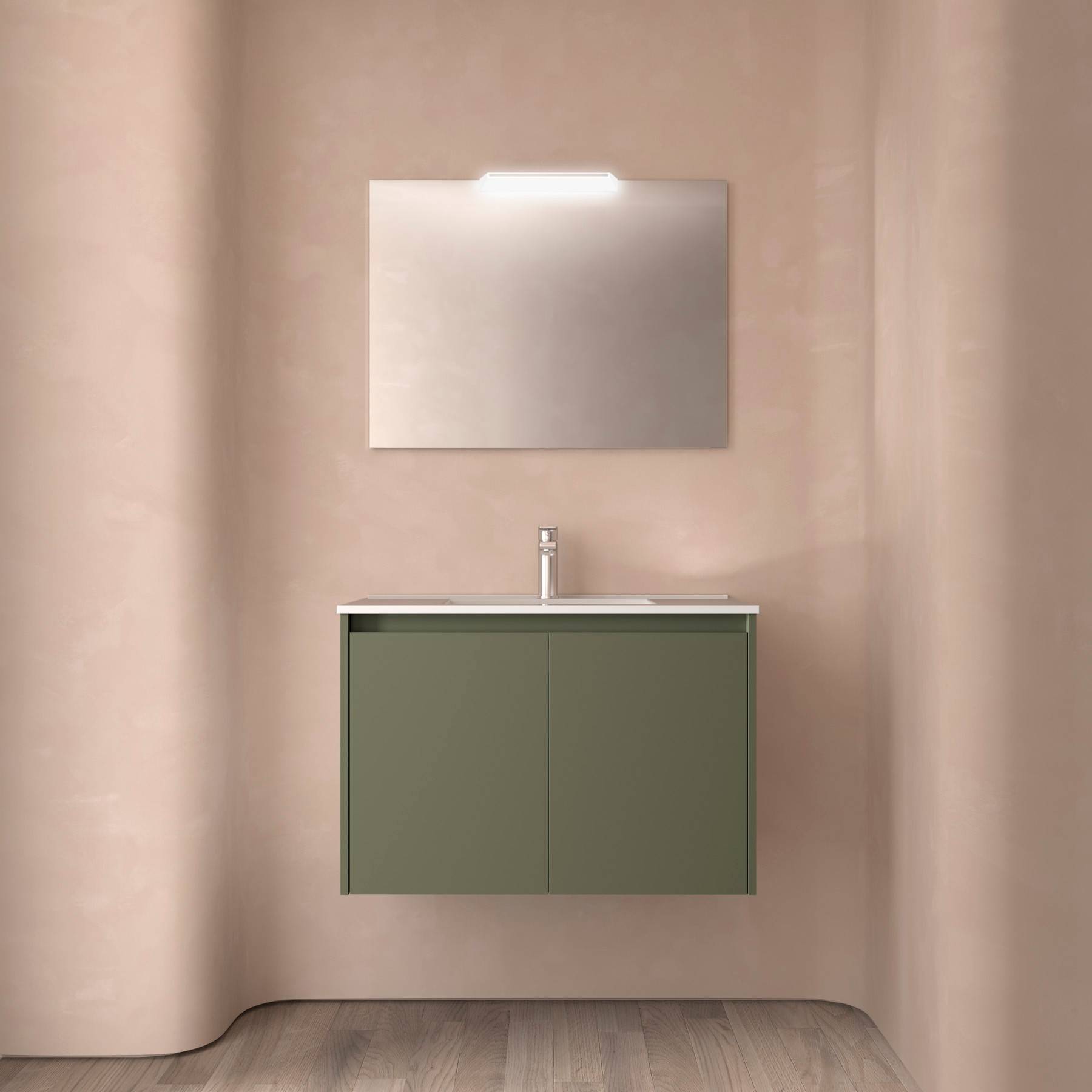 Ein minimalistisches Badezimmer zeigt einen wandmontierter Spiegel über einem modernen Waschbecken mit elegantem Wasserhahn und grünem Schrank, vor blassrosa Wänden.
