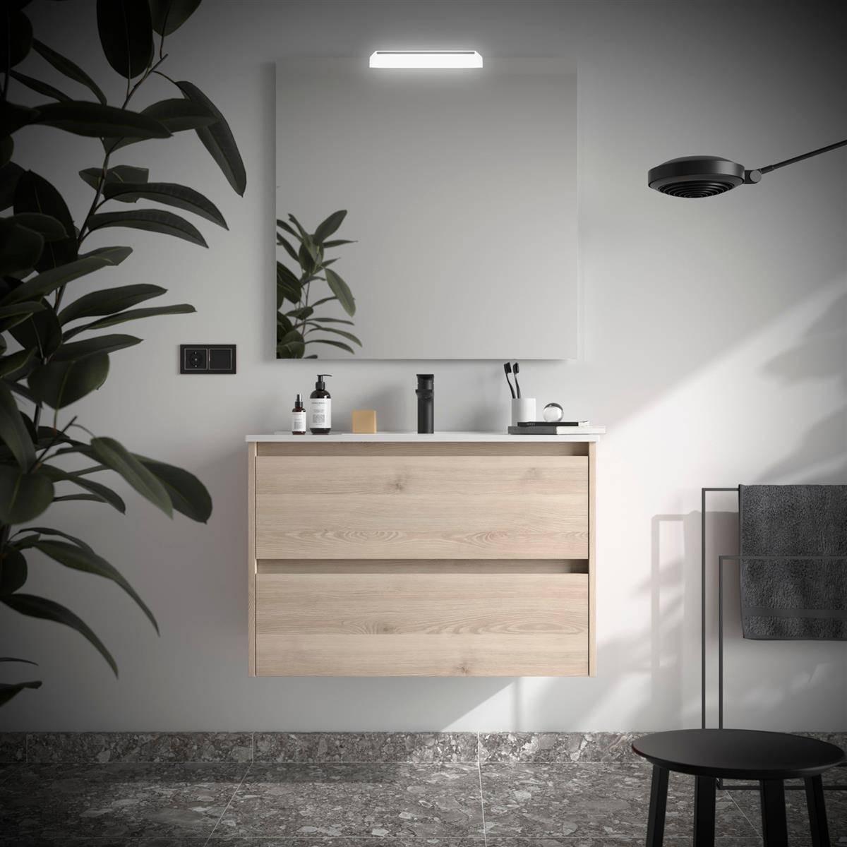 Modernes Badezimmer mit schwebendem Waschtisch aus hellem Holz, Spiegel, Wandleuchte, Handtuchhalter und schwarzem Hocker; eine Pflanze rahmt die Szene teilweise ein.