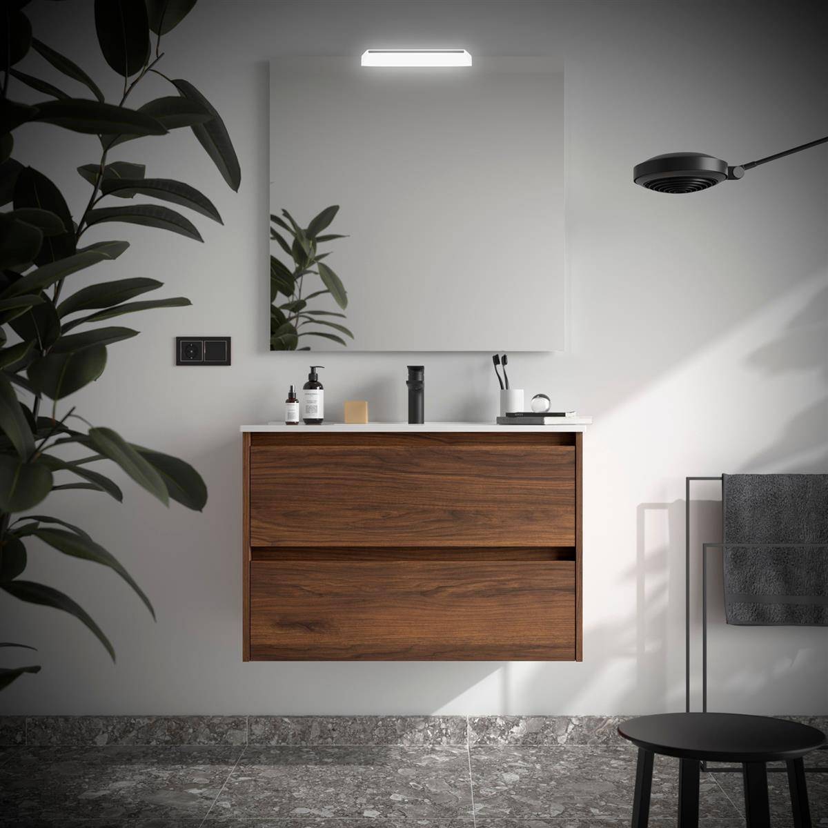 Modernes Badezimmer mit schwebendem Holzwaschtisch, rechteckigem Spiegel, Wandleuchte, Badezimmerzubehör auf der Arbeitsplatte, schwarzem Handtuchhalter, Duschkopf und Blattwerk einer Pflanze im Vordergrund.