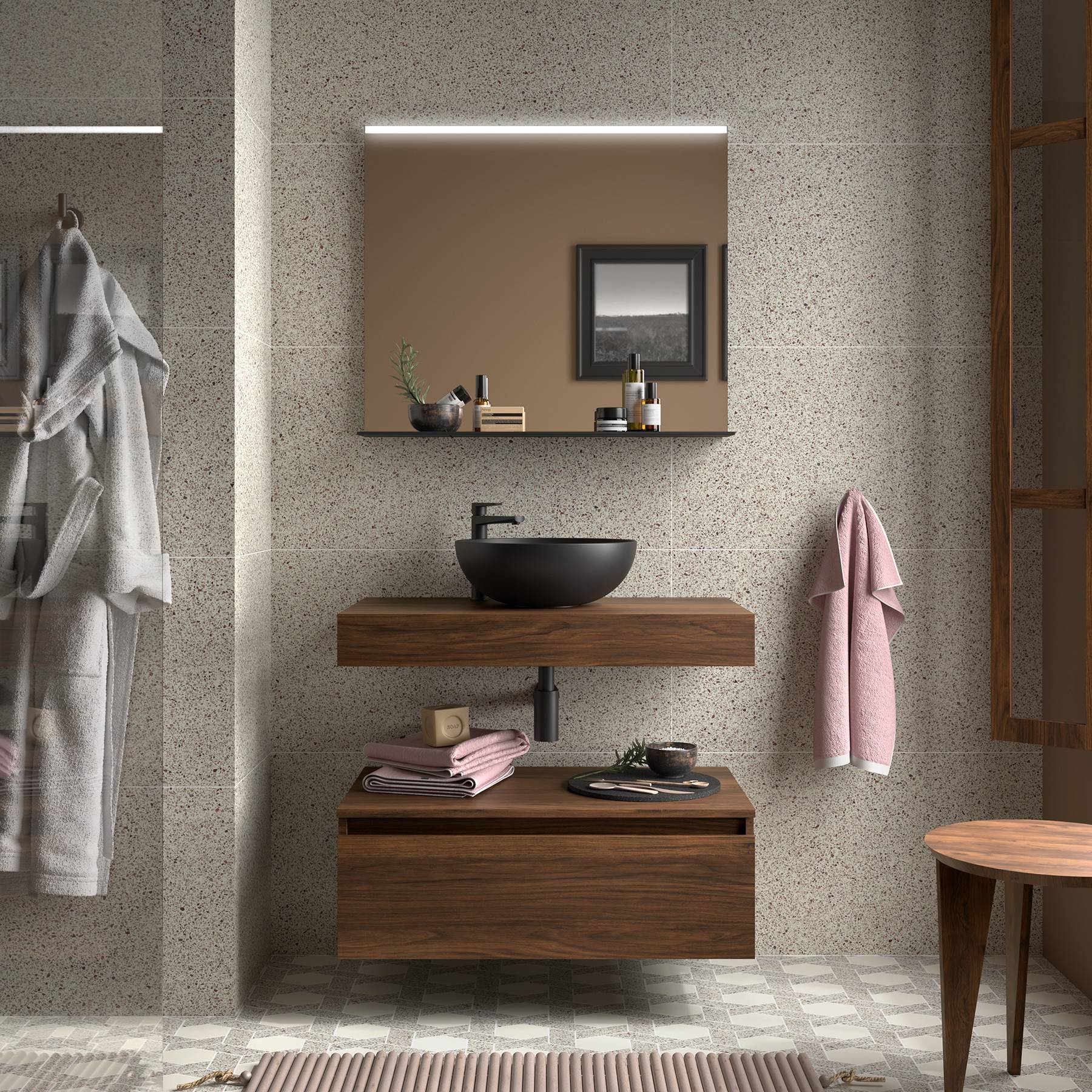 Ein modernes Badezimmer mit einer grauen gefliesten Wand, Holzwaschtisch, dunklem Aufsatzbecken und rundem Spiegel. Gefaltete Handtücher und Toilettenartikel sind ordentlich angeordnet.