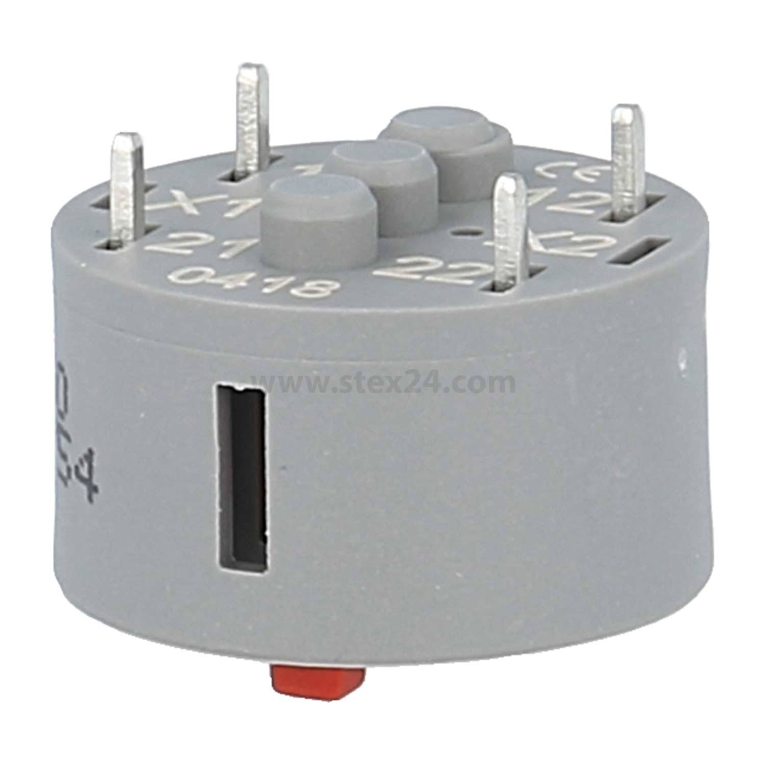 Ein grauer elektronischer Bauteil mit zwei Reihen von Metallstiften auf der Oberseite, beschriftet mit C1, C2, X1, X2 und zusätzlichen numerischen Details.