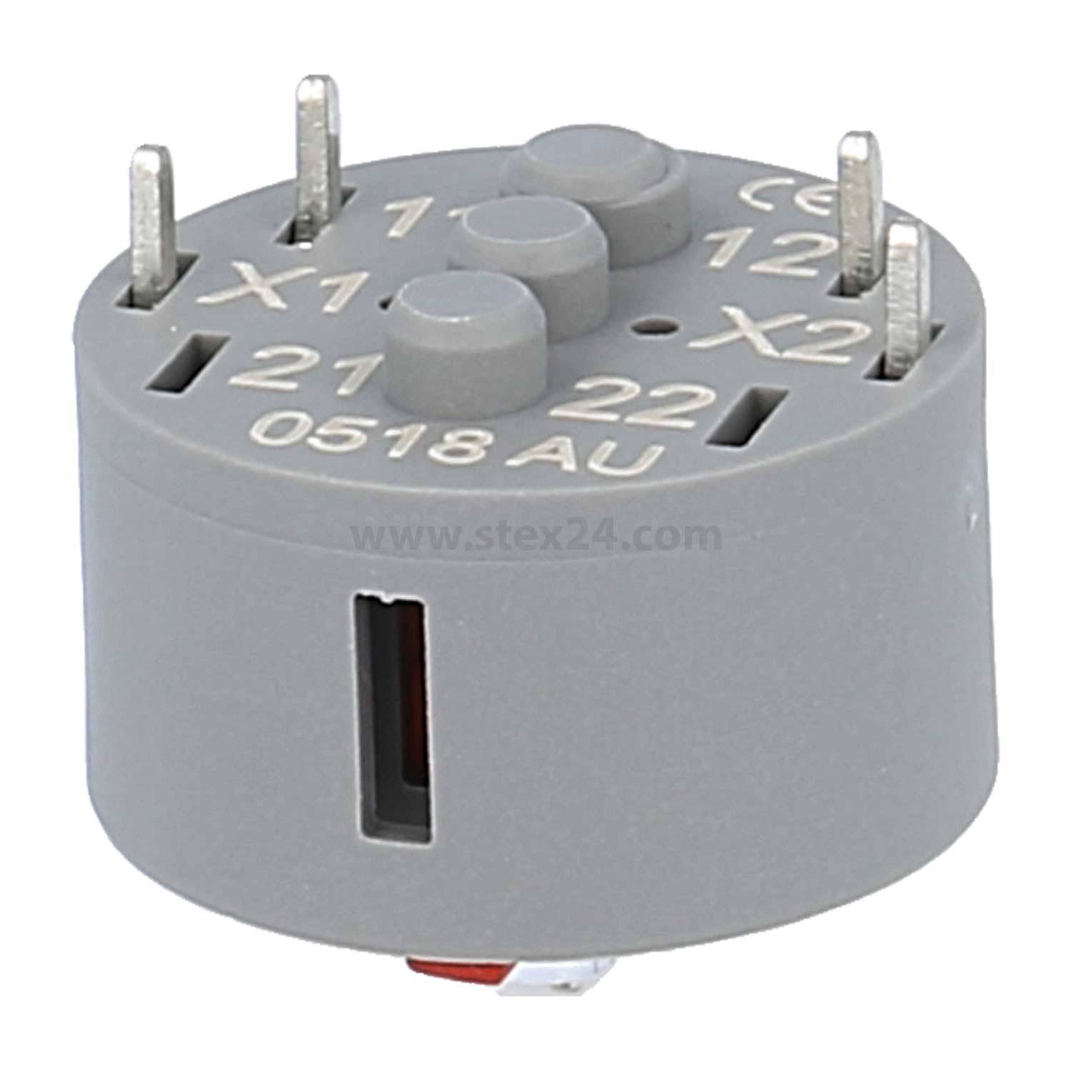 Eine graue, zylindrische elektronische Komponente mit mehreren Metallstiften oben und eingraviertem Text 'X1, X2, 0518 AU' auf ihrer Oberfläche.