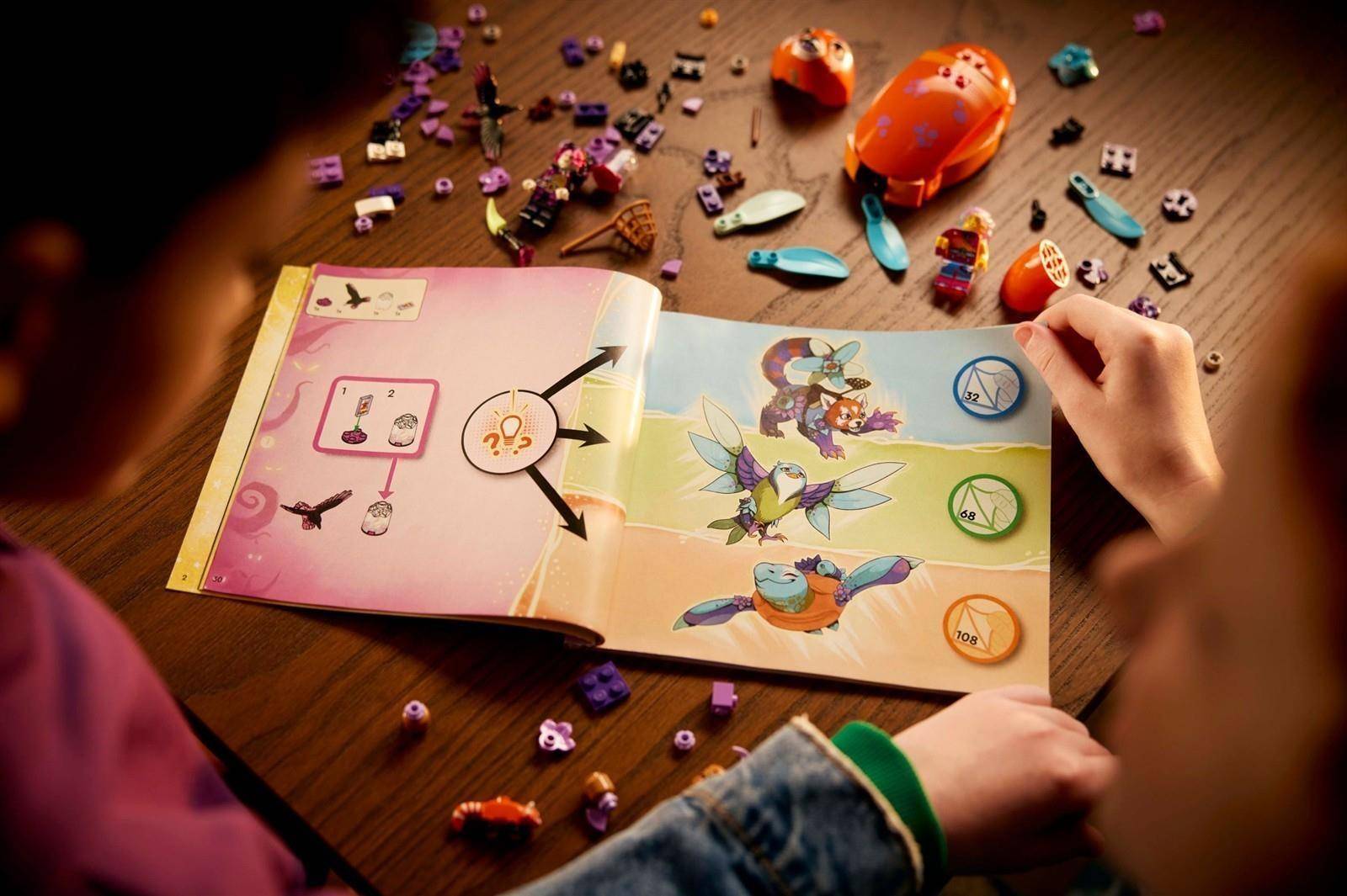 Ein Kind öffnet ein buntes Bilderbuch auf einem Tisch, mit verstreuten Spielzeugen herum und einer Hand, die die Seite umblättert.