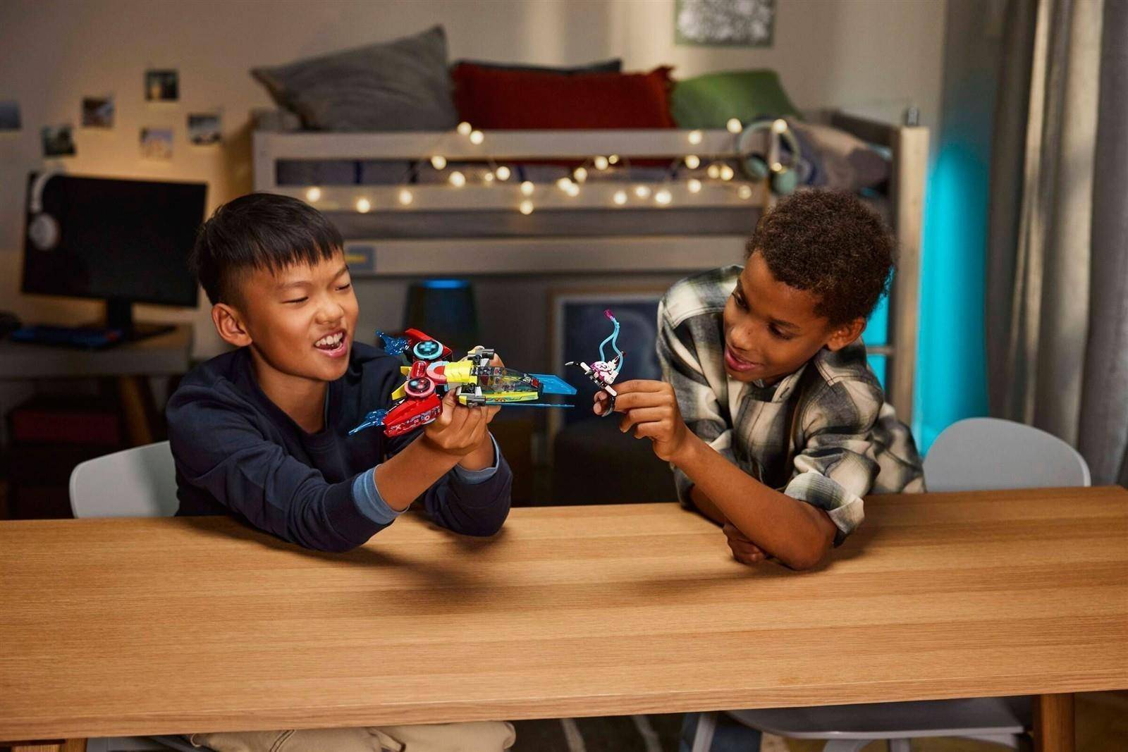 Zwei Jungen an einem Tisch spielen mit bunten Spielfiguren in einem gemütlichen Schlafzimmer, lächeln und schauen sich gegenseitig an.