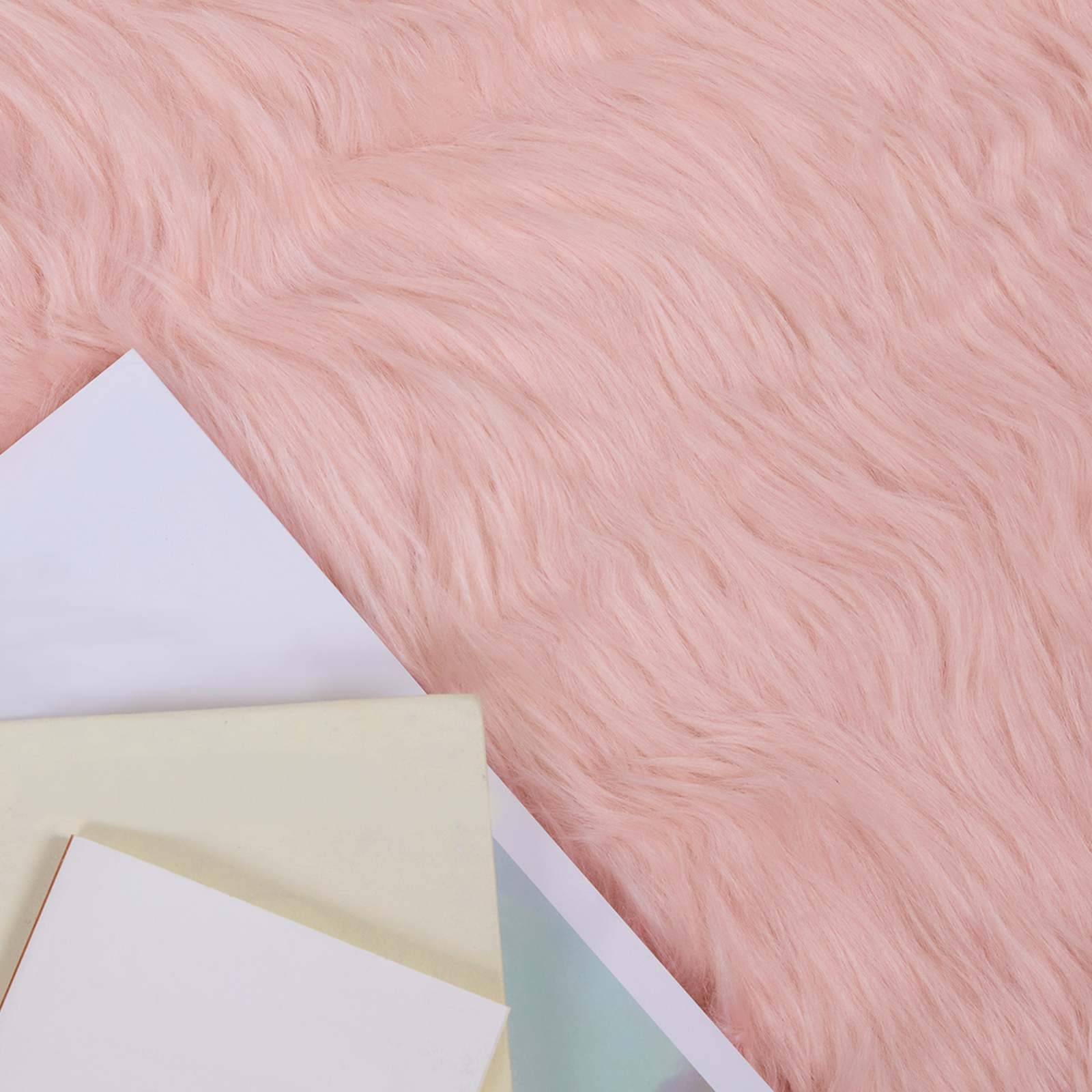 Ein weiches rosa Fellhintergrund mit überlappenden Blättern aus weißem, cremefarbenem und hellblauem Papier in der unteren linken Ecke.