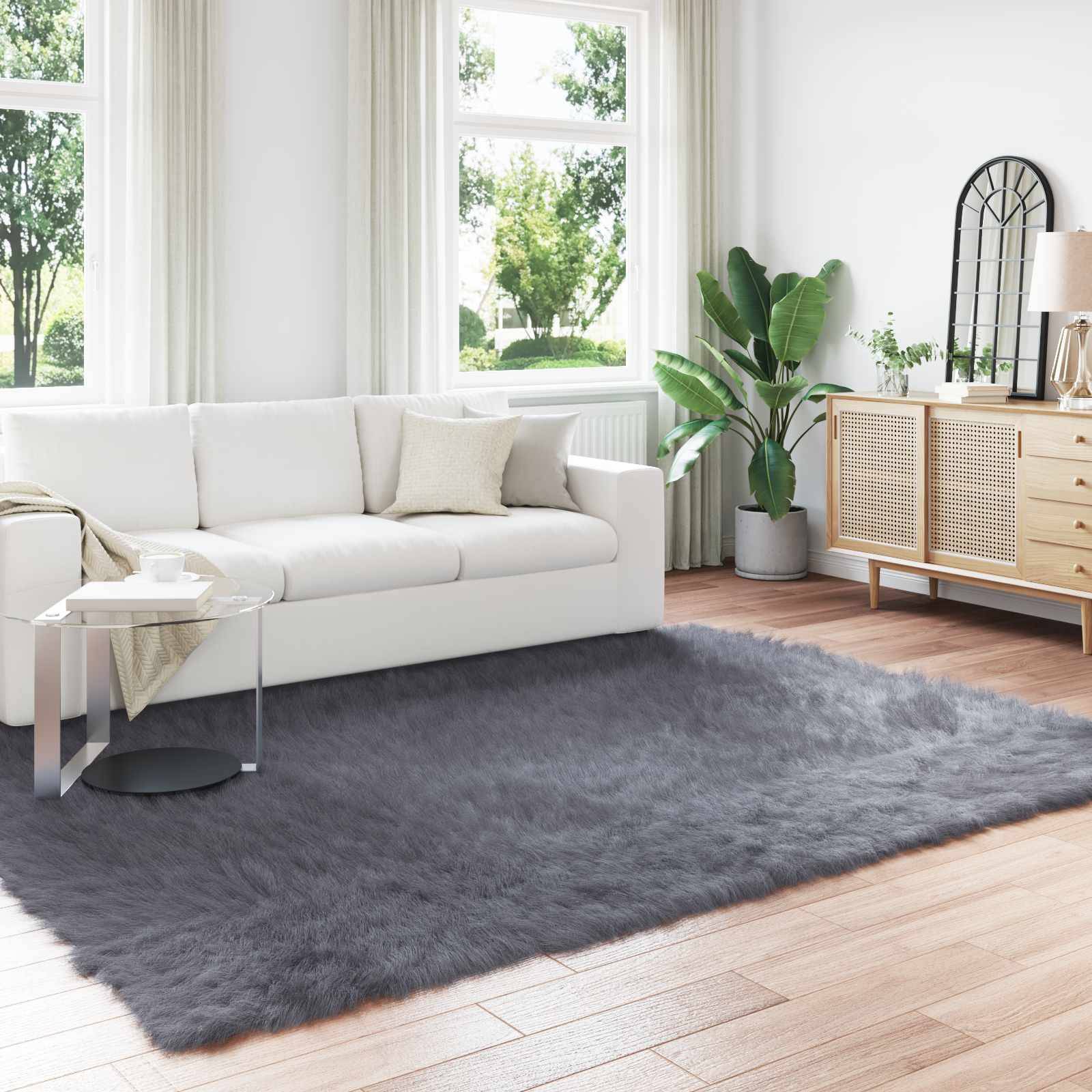 Ein modernes Wohnzimmer mit einem weißen Sofa, einer großen Pflanze und einem hölzernen Sideboard. Weiches graues Teppich und natürliches Licht durch große Fenster.