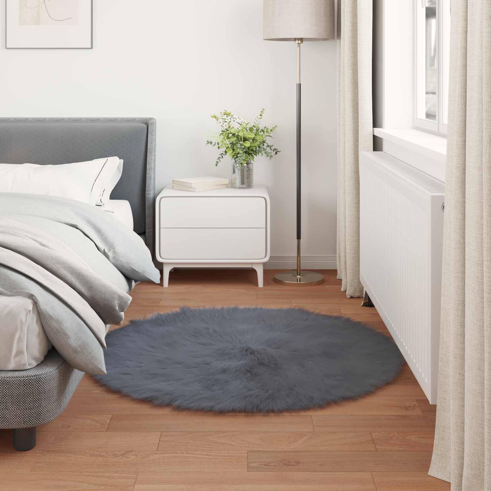 Ein modernes Schlafzimmer mit einem ordentlich gemachten Bett, grauem Kopfende, rundem grauem Teppich, Nachttisch mit einer Pflanze und einer Lampe neben einem hellen Fenster.