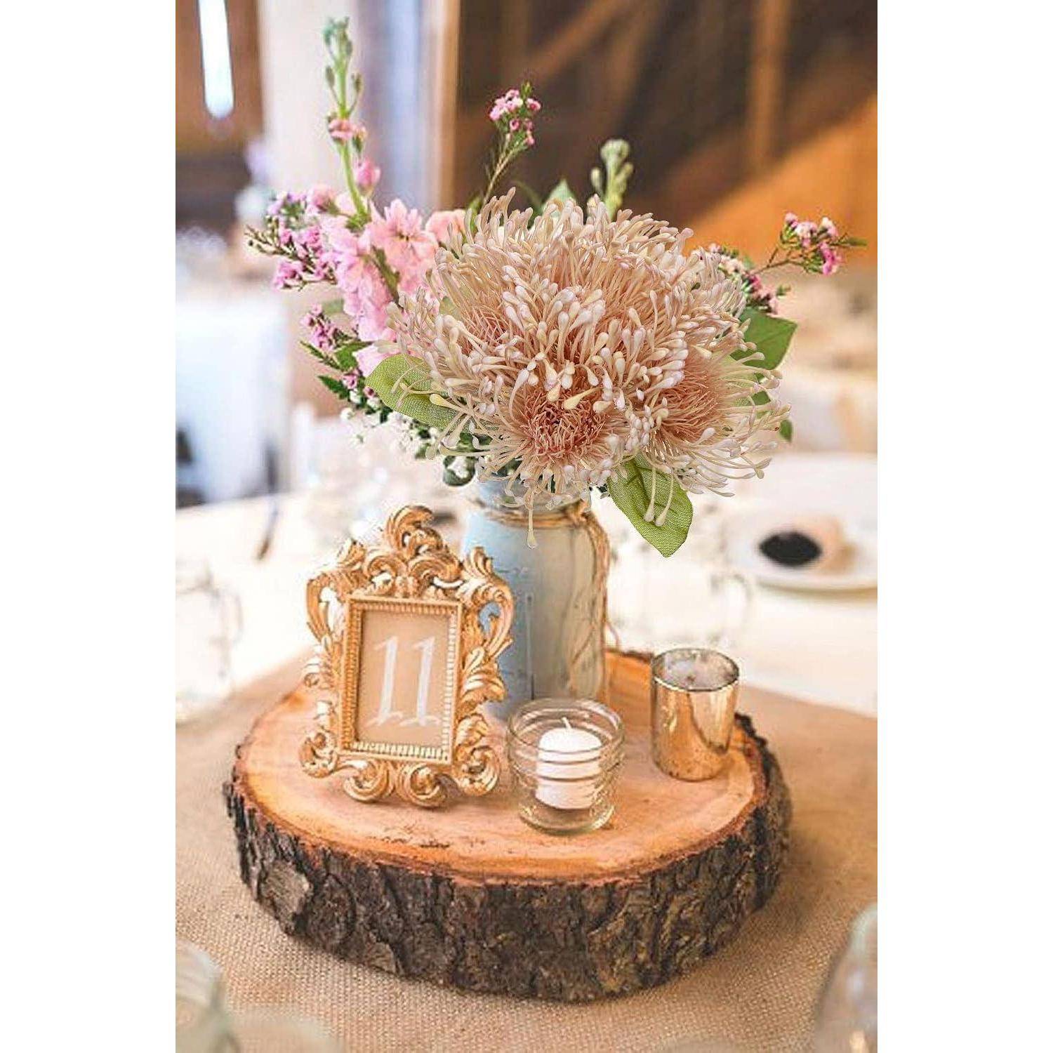 Tischdekoration mit rosa Blumen in einem Glas, einem gerahmten Schild mit der Zahl '11', einer Kerze und einer kleinen metallfarbenen Vase auf einem Holzbrett.
