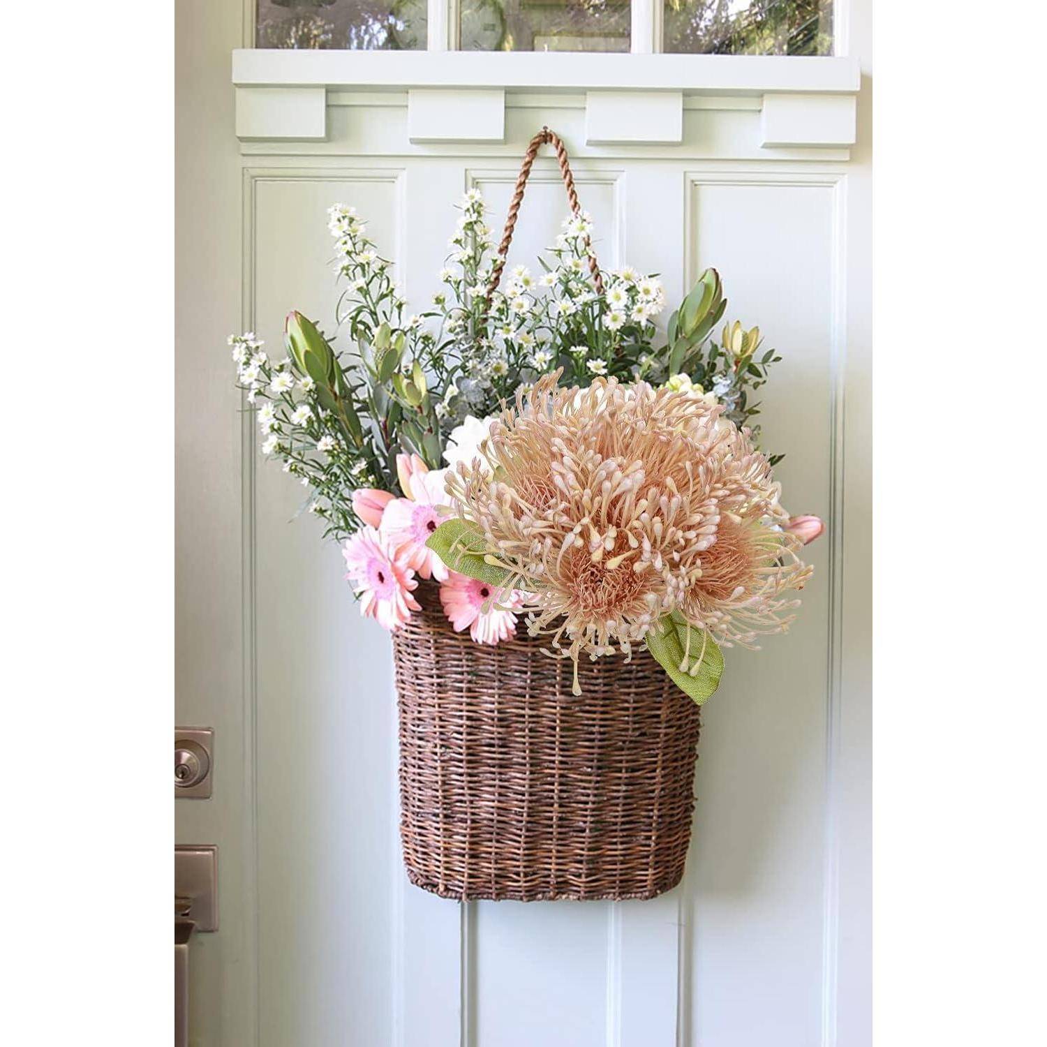 Ein Flechtkorb, gefüllt mit verschiedenen rosa und weißen Blumen, hängt an einer hellfarbenen Tür und verleiht ihr einen einladenden und frischen Anblick.