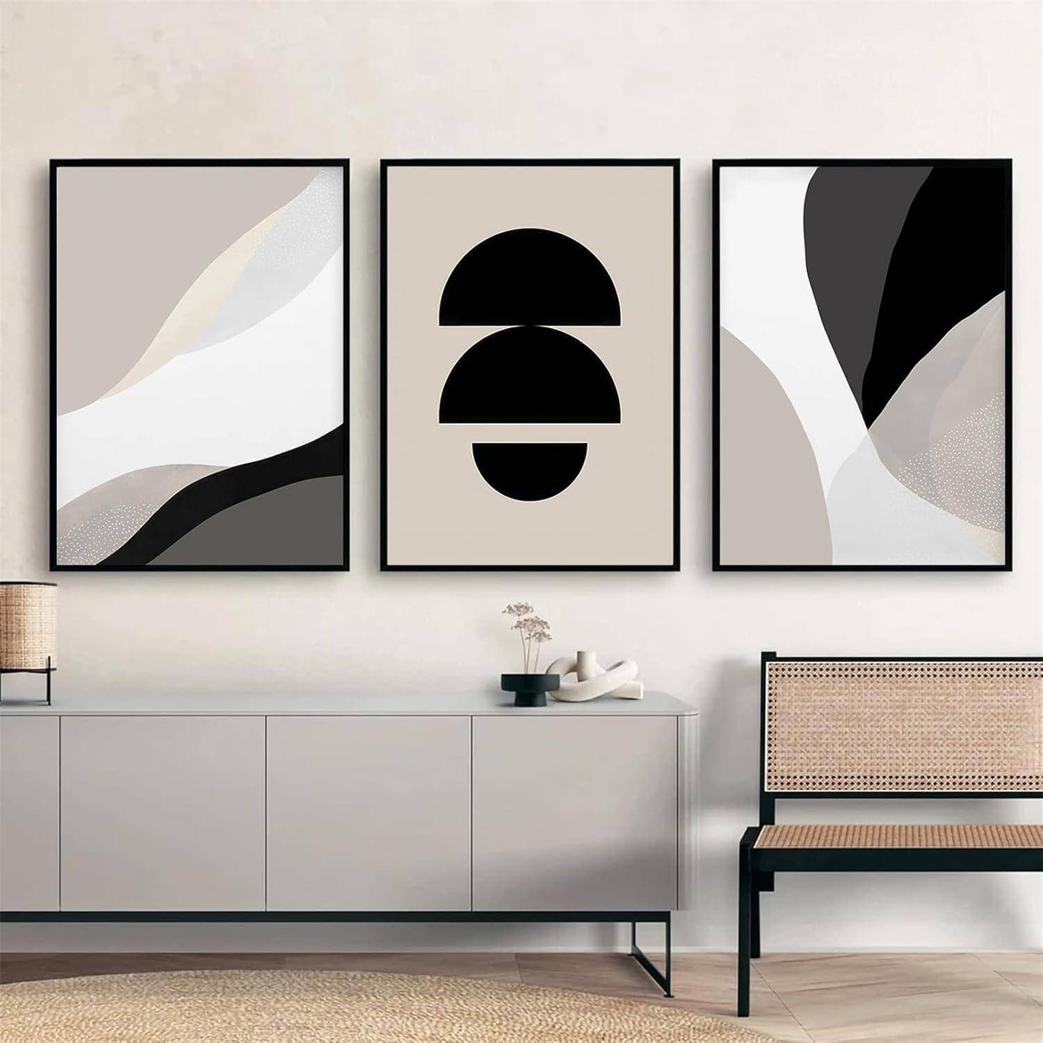 Drei abstrakte Kunstwerke in Schwarz, Weiß und Beige hängen über einer modernen Konsole und einem Stuhl und verleihen dem Raum eine zeitgemäße Note.