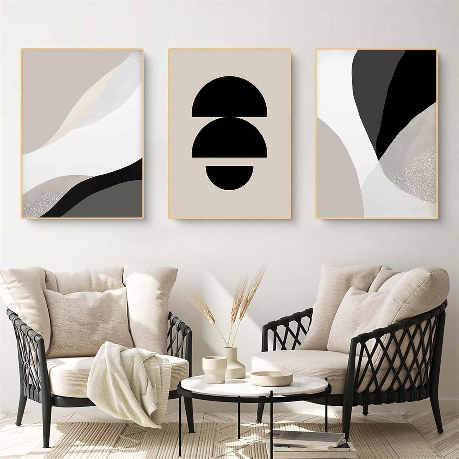 Ein Wohnzimmer mit zwei beigen Sesseln, einem runden Couchtisch und drei abstrakten Kunstwerken in Schwarz, Weiß und Beige an der Wand.