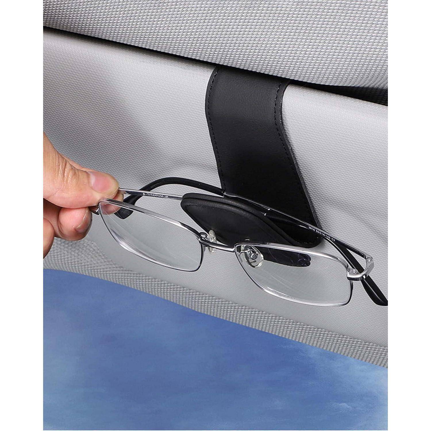 Eine Hand legt eine Brille in einen schwarzen Clip, der an der Sonnenblende eines Autos befestigt ist, um sie sicher und leicht zugänglich während der Fahrt zu halten.