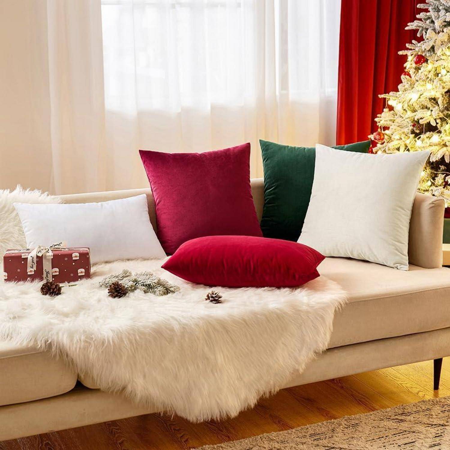 Eine gemütliche Wohnzimmerszene mit einem beigen Sofa, das mit festlichen roten, weißen und grünen Kissen und einer flauschigen weißen Decke geschmückt ist, neben einem Weihnachtsbaum.