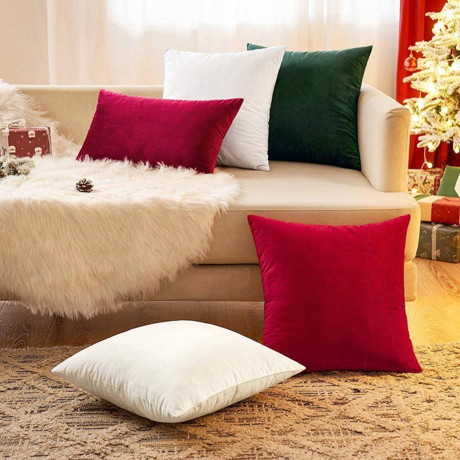 Eine gemütliche Wohnzimmerszene mit einem beigen Sofa, geschmückt mit roten, grünen und weißen Kissen. Ein Weihnachtsbaum und Geschenkkartons befinden sich in der Nähe und erzeugen eine festliche Atmosphäre.