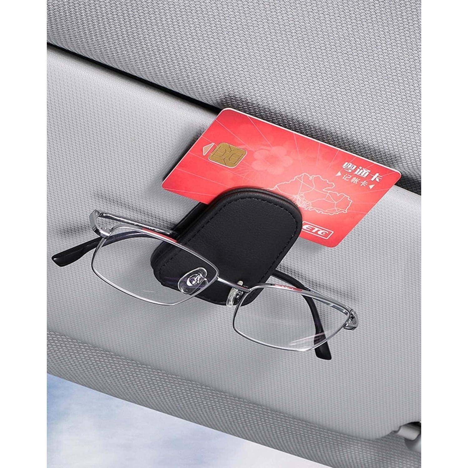 Brillenhalter, der an einem Sonnenblendenspiegel eines Autos befestigt ist und eine rote Karte mit goldenem Chip hält, vor einem grauen Innenraum-Hintergrund.