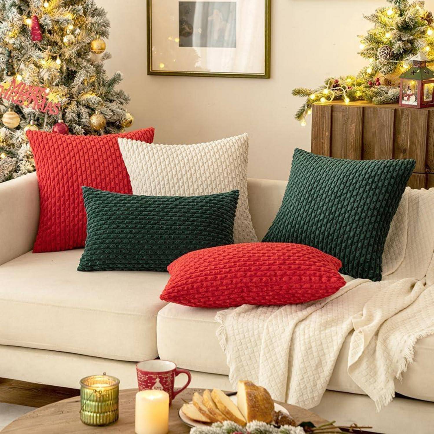 Ein gemütliches Wohnzimmer, weihnachtlich dekoriert, mit einem Sofa, das mit roten, grünen und weißen strukturierten Kissen geschmückt ist. Im Hintergrund steht ein beleuchteter Weihnachtsbaum.