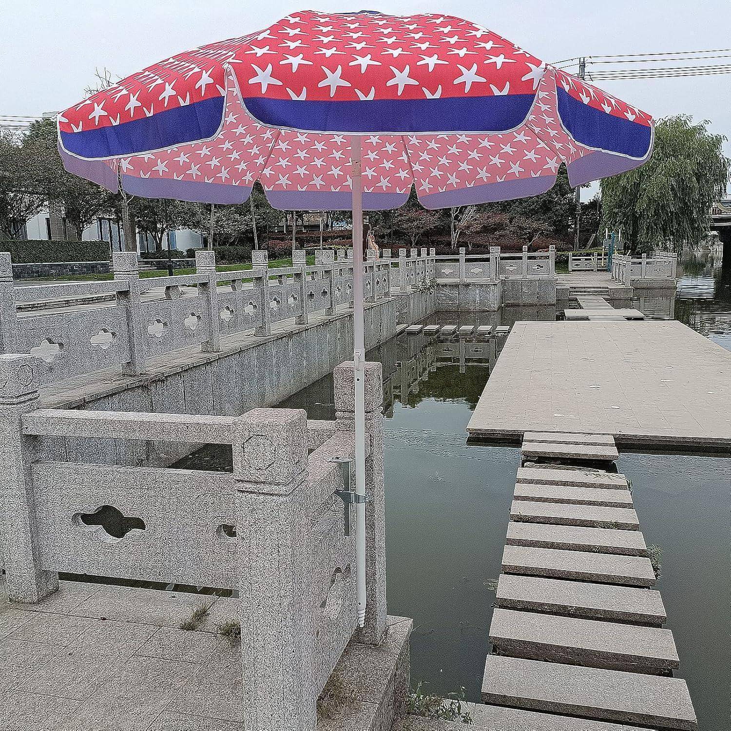 Eine Steinbrücke mit dekorativen Geländern überquert einen ruhigen Teich. Ein rot-blauer Regenschirm mit Sternenmuster spendet Schatten auf dem Weg.