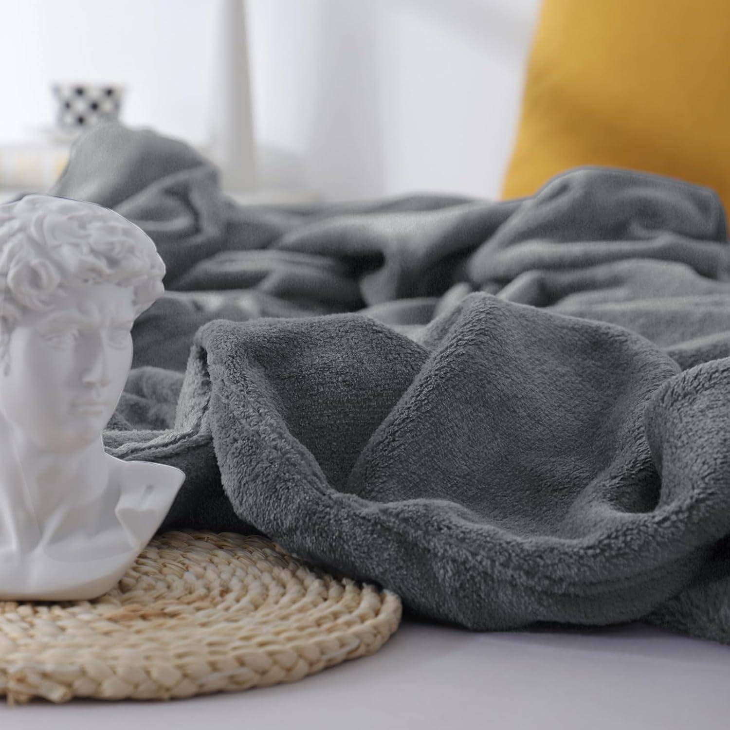 Eine weiße Marmorbüste steht auf einer gewebten Matte neben einer grauen Decke, mit einem gelben Kissen, das im Hintergrund zu sehen ist.