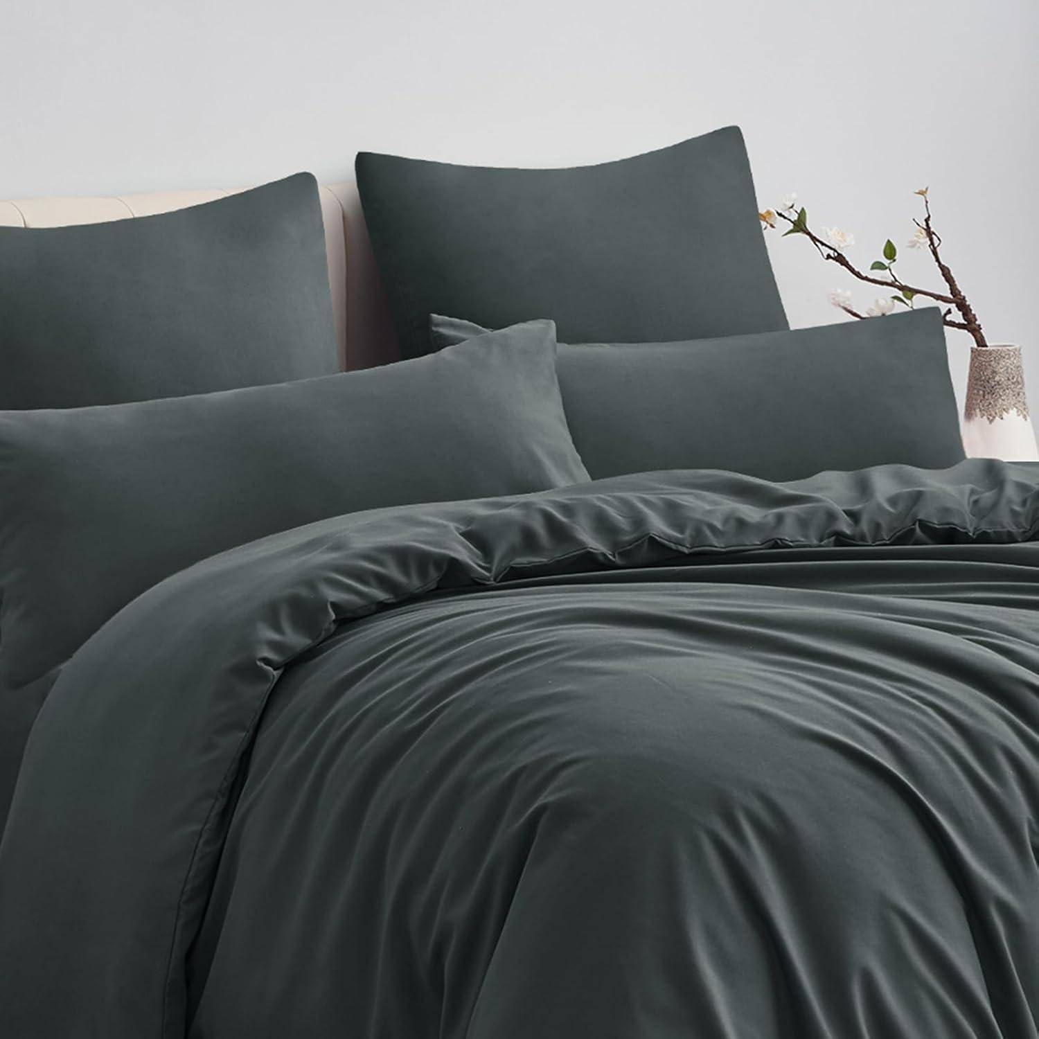 Ein sorgfältig angeordneter Satz Bettwäsche in dunklem Grau, bestehend aus einem Bettdeckenbezug, Kissen und Betttüchern, auf einem Bett mit schlichten Dekoelementen präsentiert.