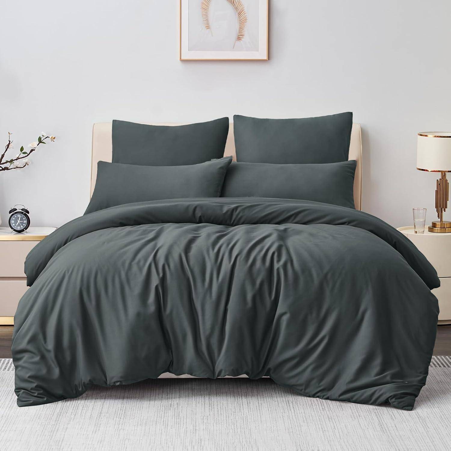 Ein sauber gemachtes Bett mit dunkelgrauer Bettwäsche, zwei Kissen und einem Kopfteil. Eine kleine Lampe und Dekoartikel stehen auf Nachttischen.